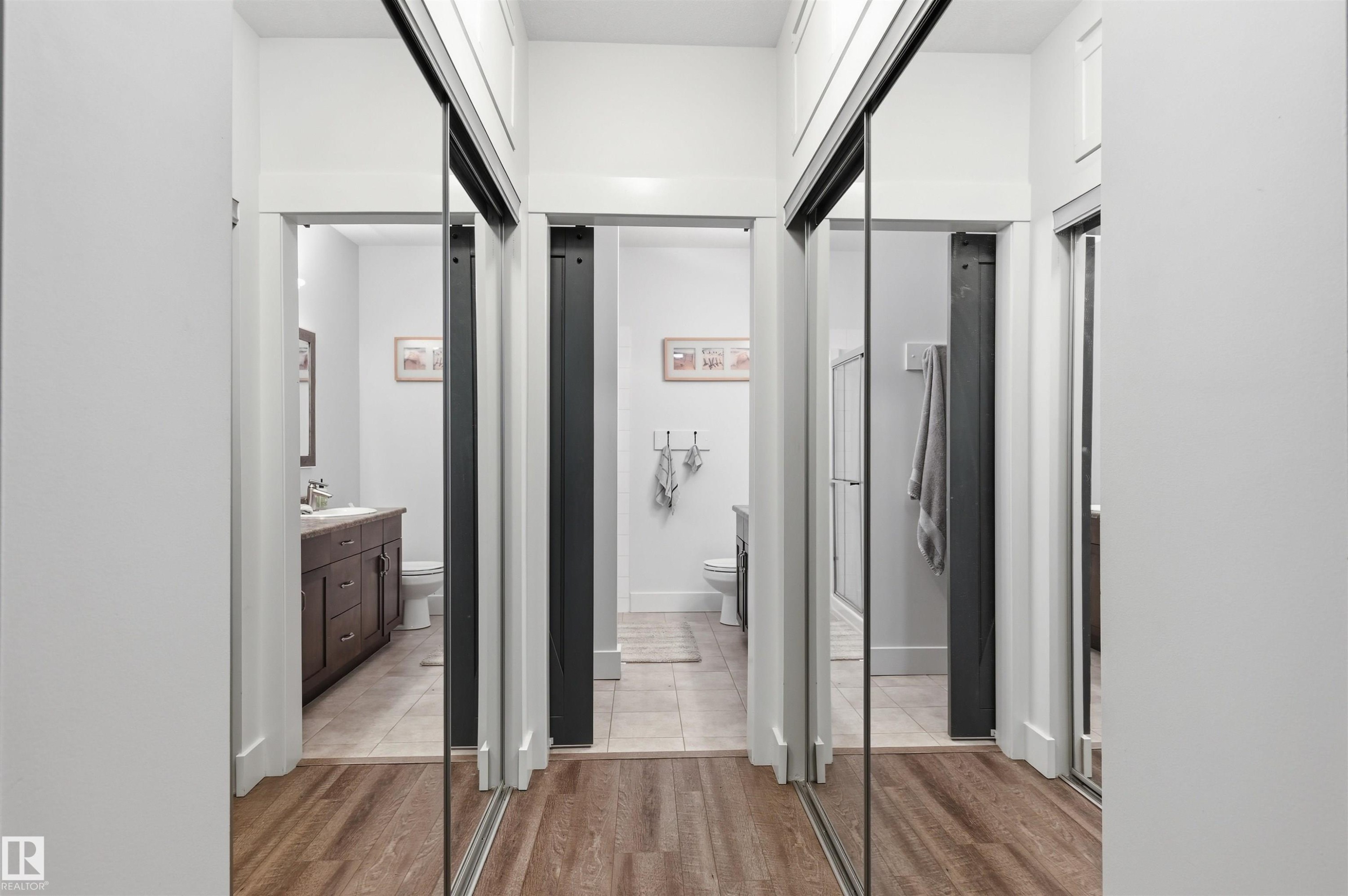 Hallway with wood-finish flooring and three sets of mirrored sliding closet doors - 217 2503 Hanna Crescent, Edmonton, AB