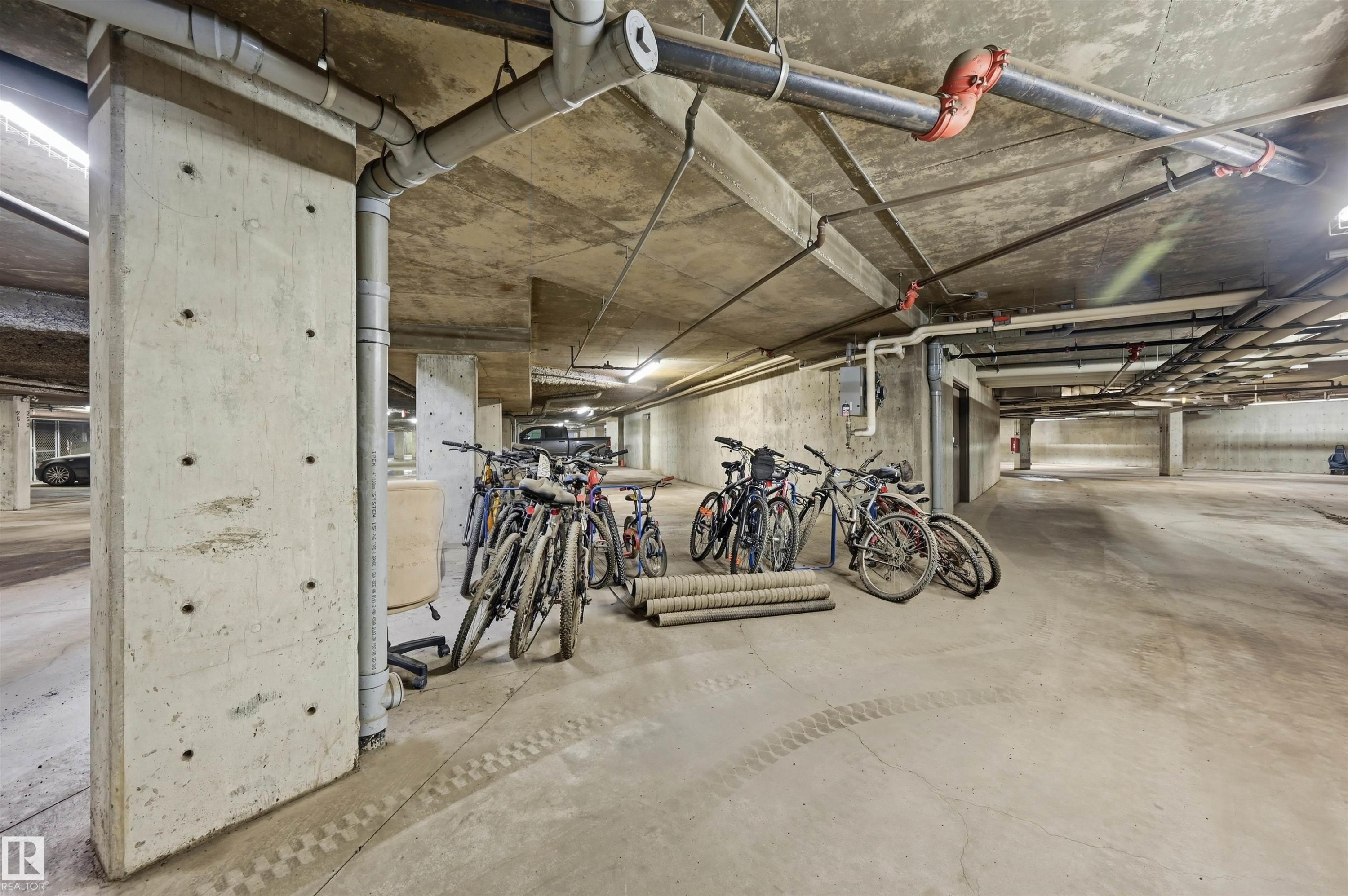 Underground parking area featuring exposed concrete structural elements and overhead utility piping - 217 2503 Hanna Crescent, Edmonton, AB
