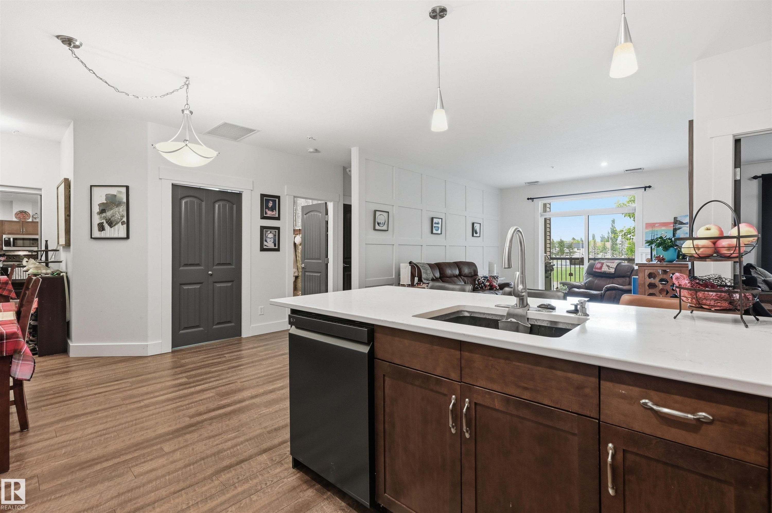 Kitchen island featuring a single-basin sink with a gooseneck faucet, integrated dishwasher, and rich wood-finish cabinetry - 217 2503 Hanna Crescent, Edmonton, AB