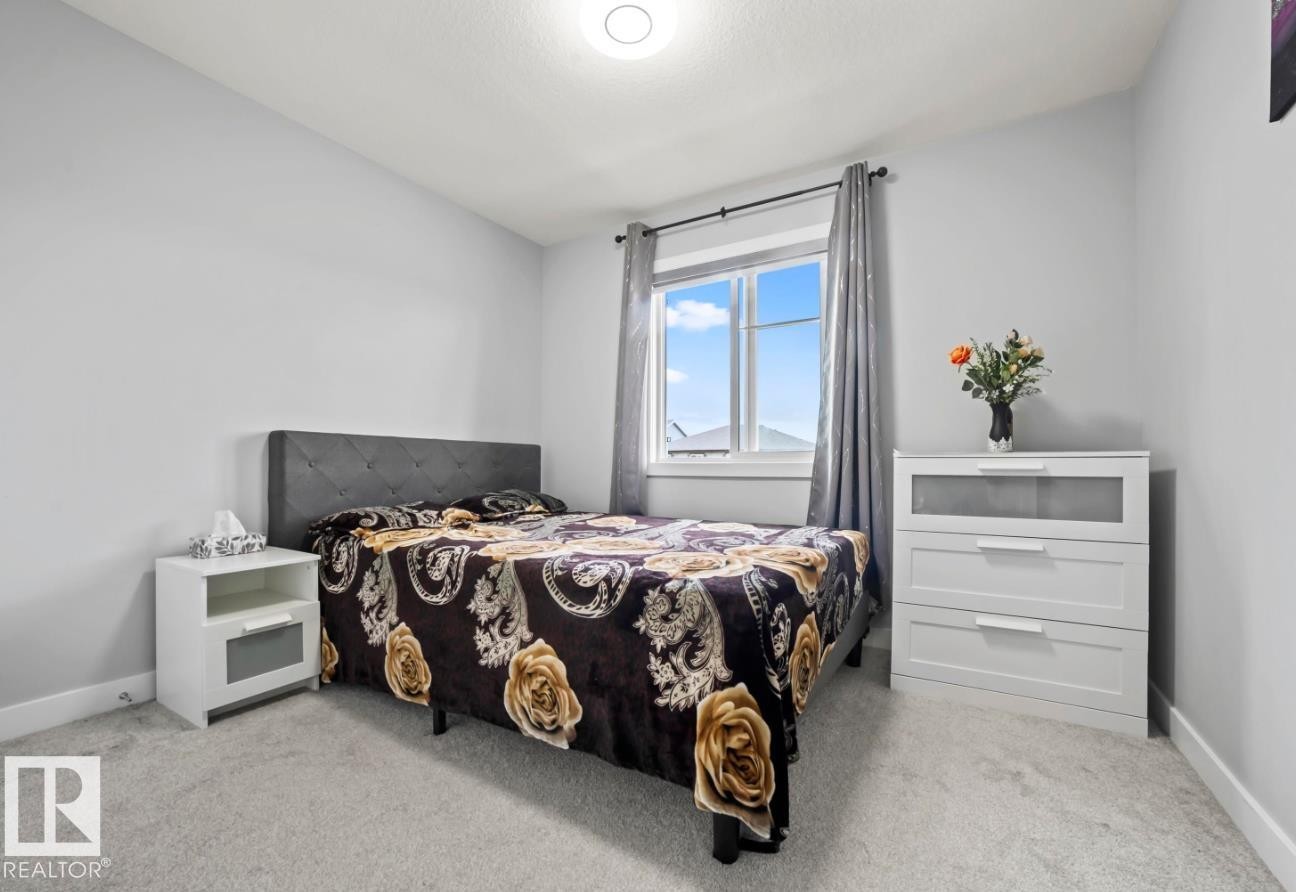 Bright bedroom featuring light gray walls, plush gray carpet, and a large window with white trim - 2153 Maple Road, Edmonton, AB