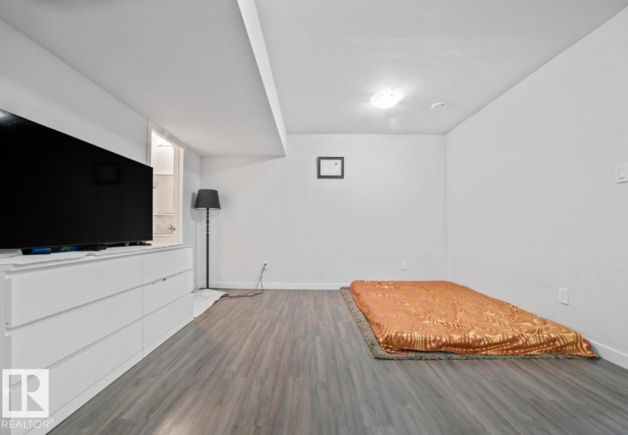 Spacious room featuring wood-finish flooring, white walls, and an overhead lighting fixture - 2153 Maple Road, Edmonton, AB