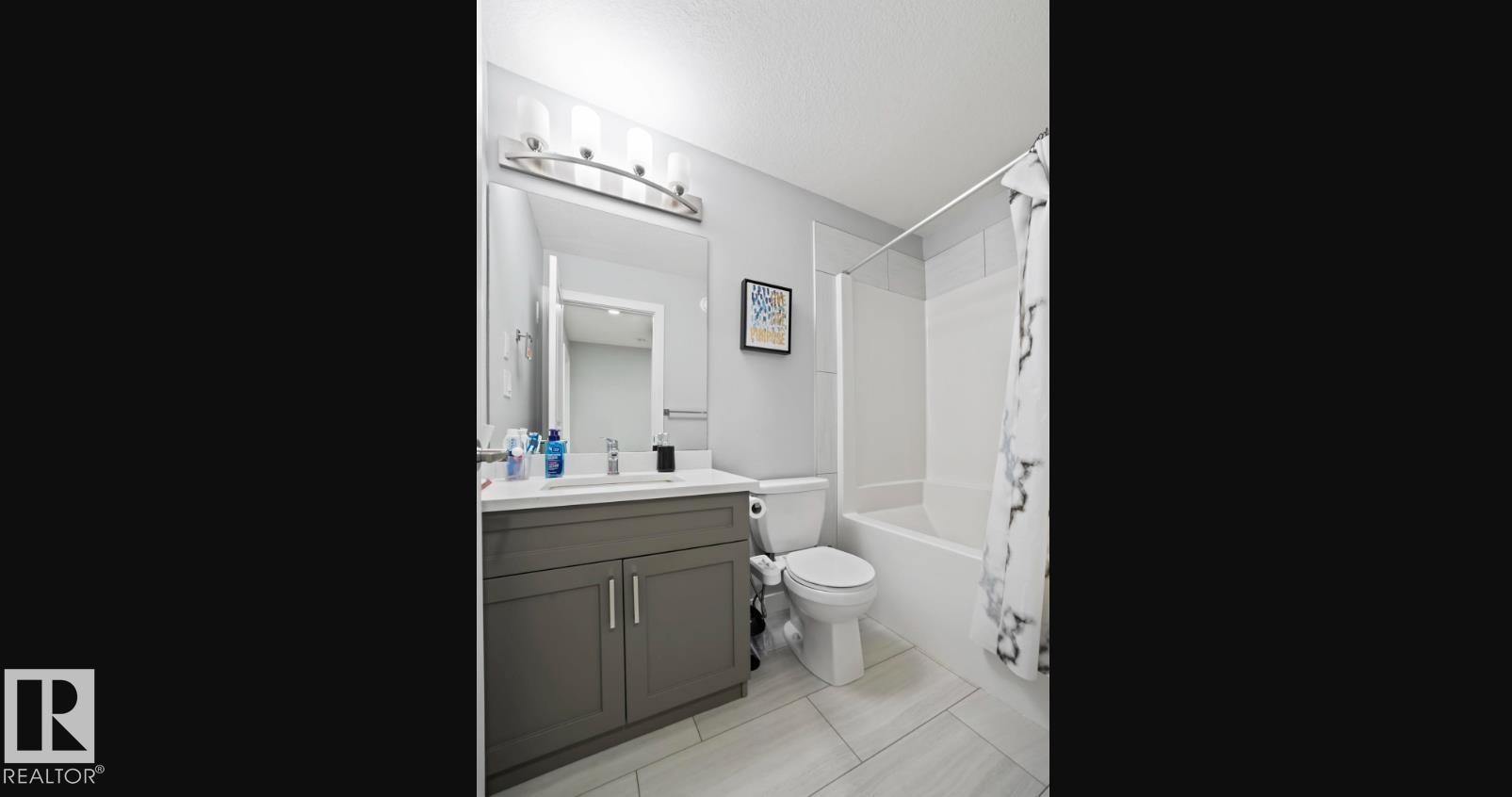 Modern bathroom featuring a single vanity with a white countertop and gray cabinetry, a white toilet, and a white bathtub with subway tile surround - 2153 Maple Road, Edmonton, AB
