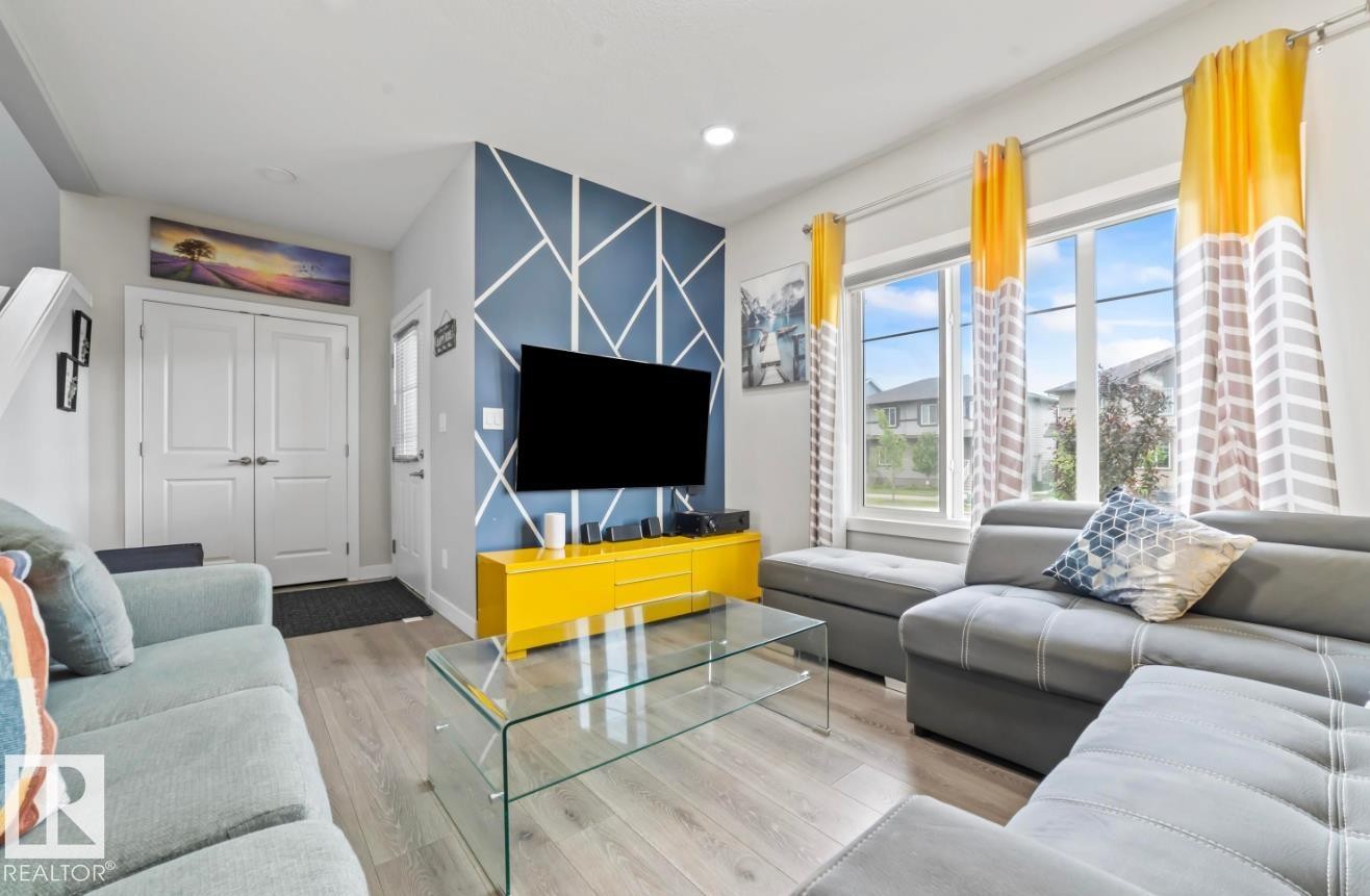 Spacious living area featuring wood-finish flooring, a geometric accent wall, and ample natural light from large windows - 2153 Maple Road, Edmonton, AB