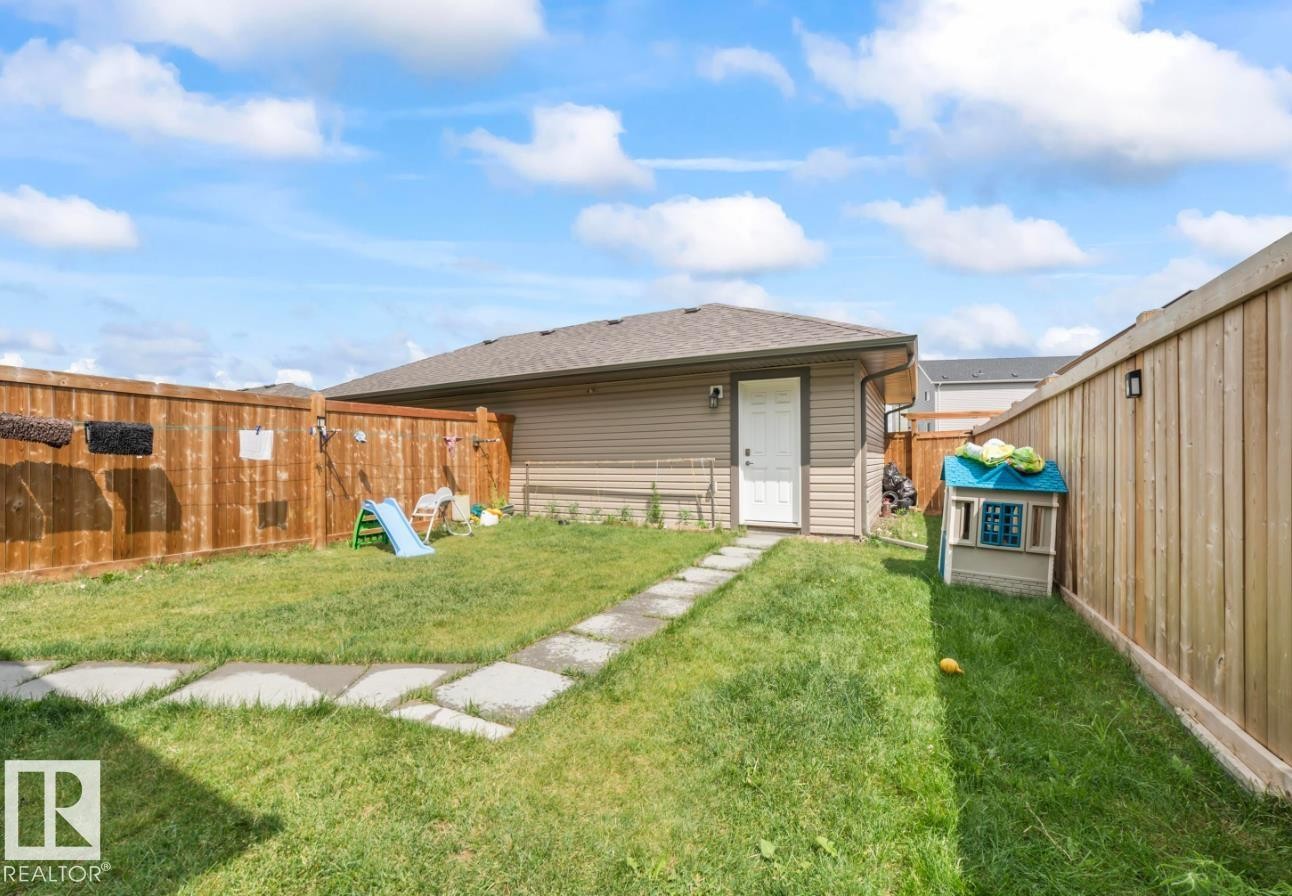 Enclosed backyard featuring a manicured lawn, stone paver pathway, and a privacy fence - 2153 Maple Road, Edmonton, AB