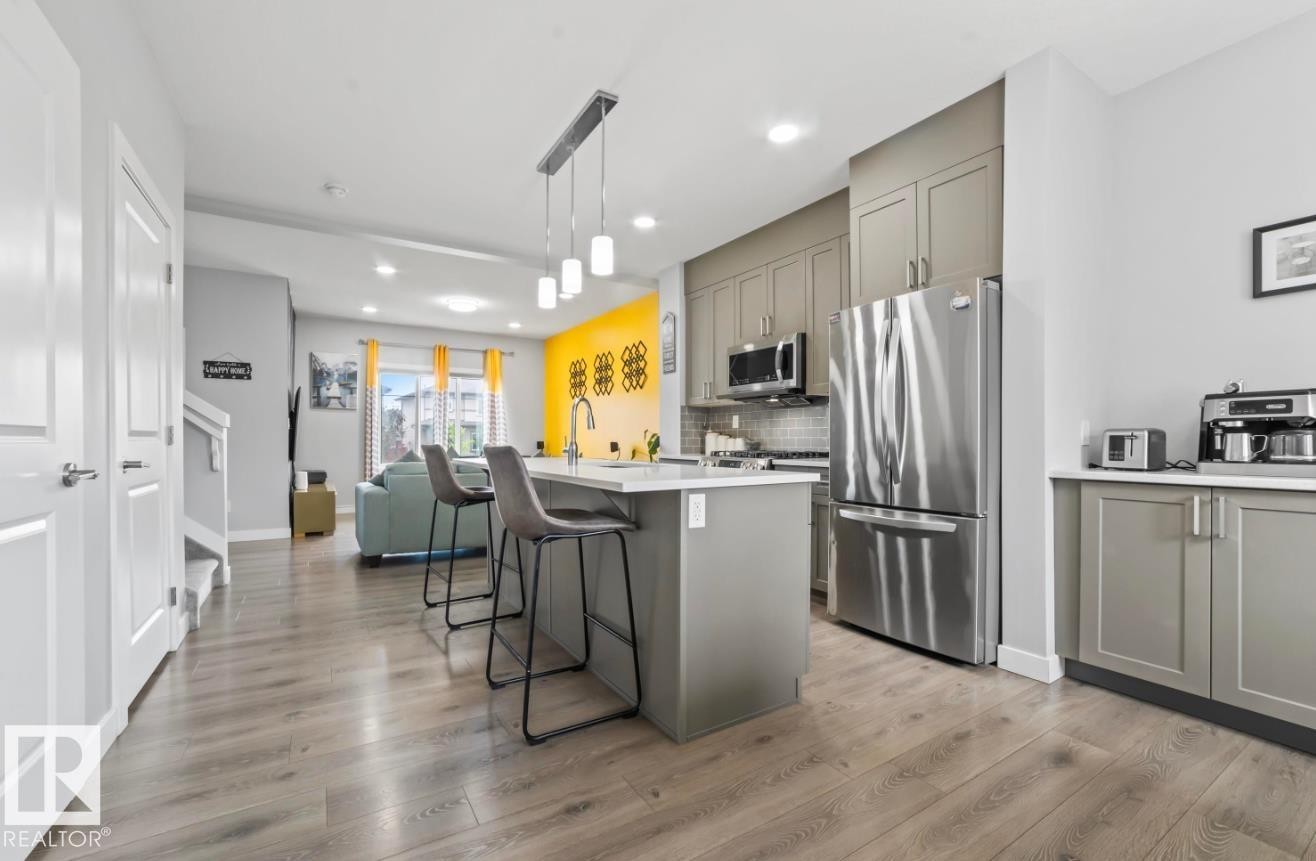 Open-concept kitchen featuring an island with seating, stainless steel appliances, grey cabinetry, and wood-finish flooring - 2153 Maple Road, Edmonton, AB