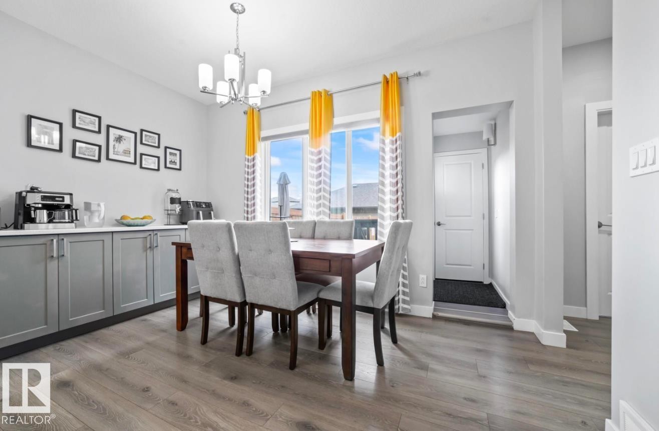 Dining area featuring wood-finish flooring, a contemporary chandelier, and a large window - 2153 Maple Road, Edmonton, AB