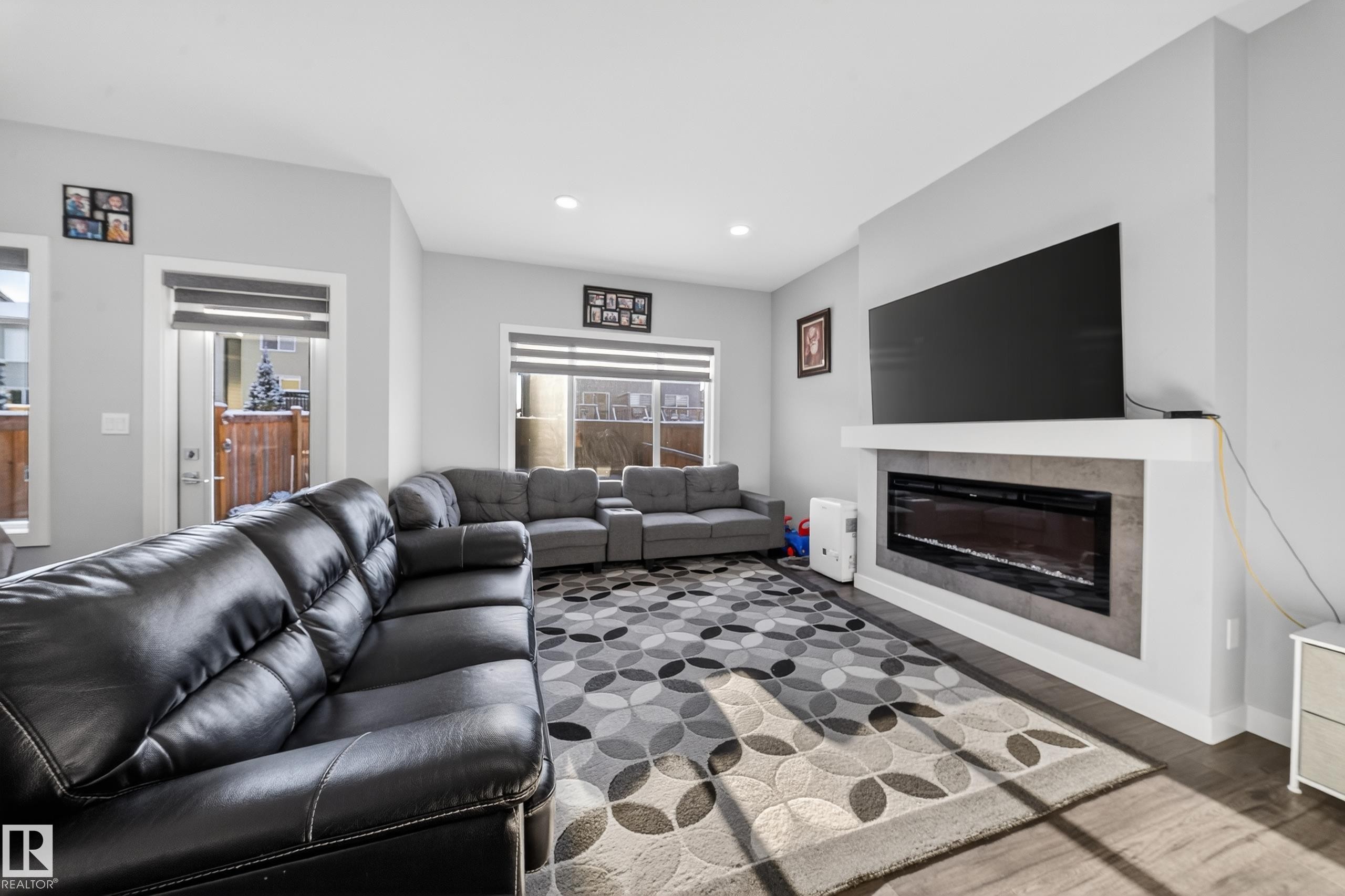 Living area featuring a modern linear electric fireplace with a stone-look surround, recessed lighting, wood-finish flooring, and light gray wall paint - 2084 Graydon Hill, Edmonton, AB