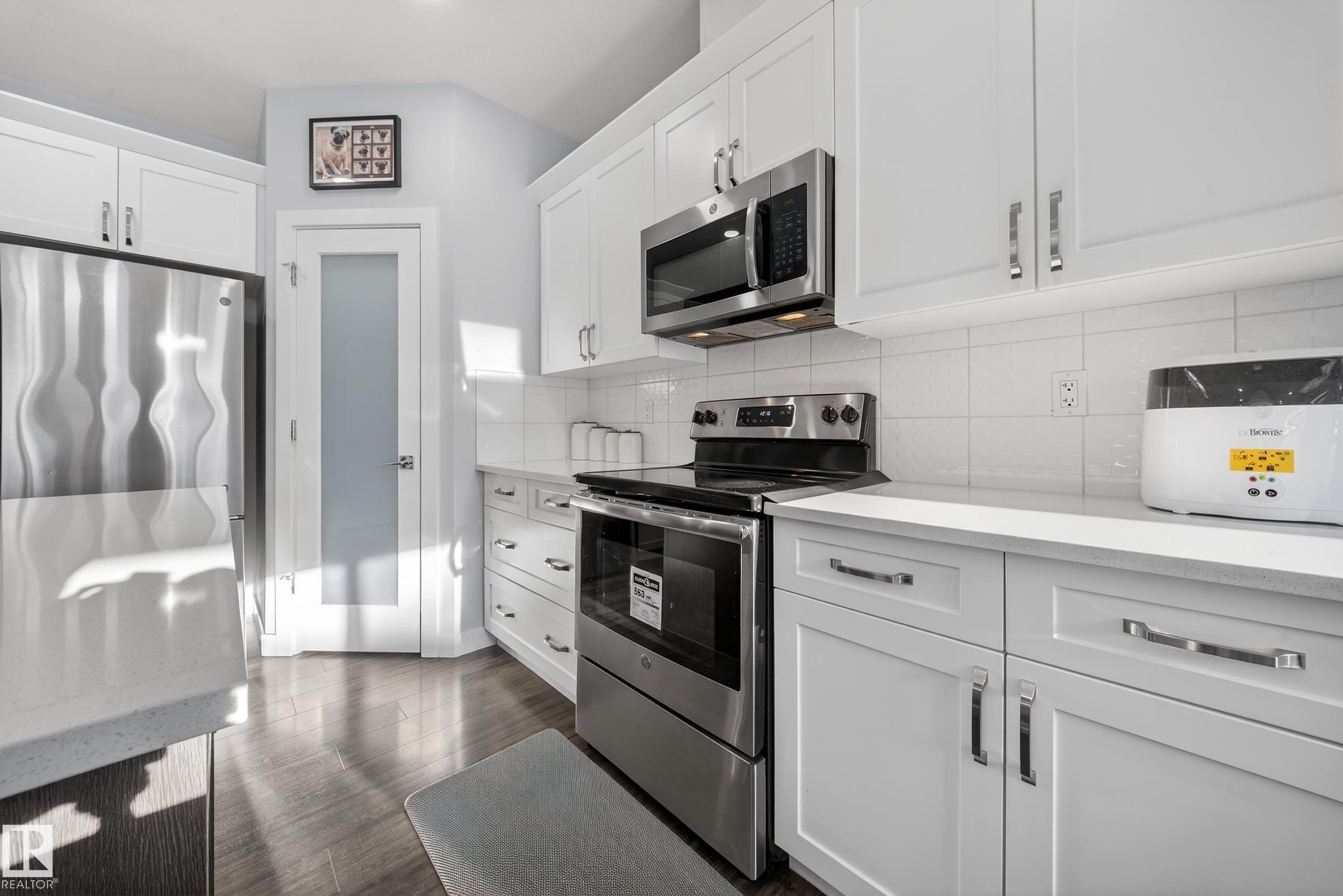 Modern kitchen featuring white cabinetry, stainless steel appliances, light countertops, and wood-finish flooring - 2084 Graydon Hill, Edmonton, AB