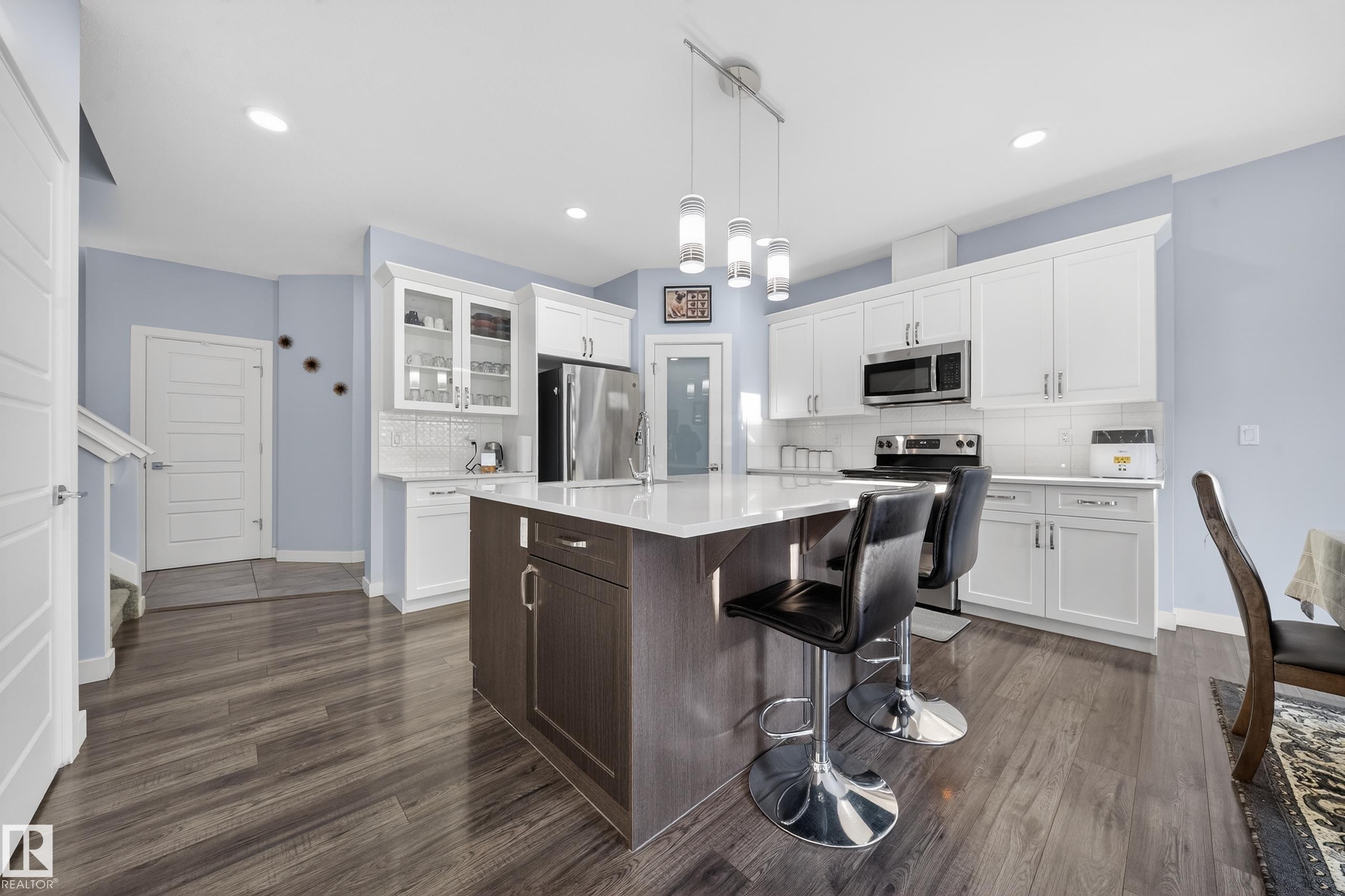 Open-concept kitchen featuring an island with counter seating, a white subway tile backsplash, stainless steel appliances, and wood-finish flooring - 2084 Graydon Hill, Edmonton, AB