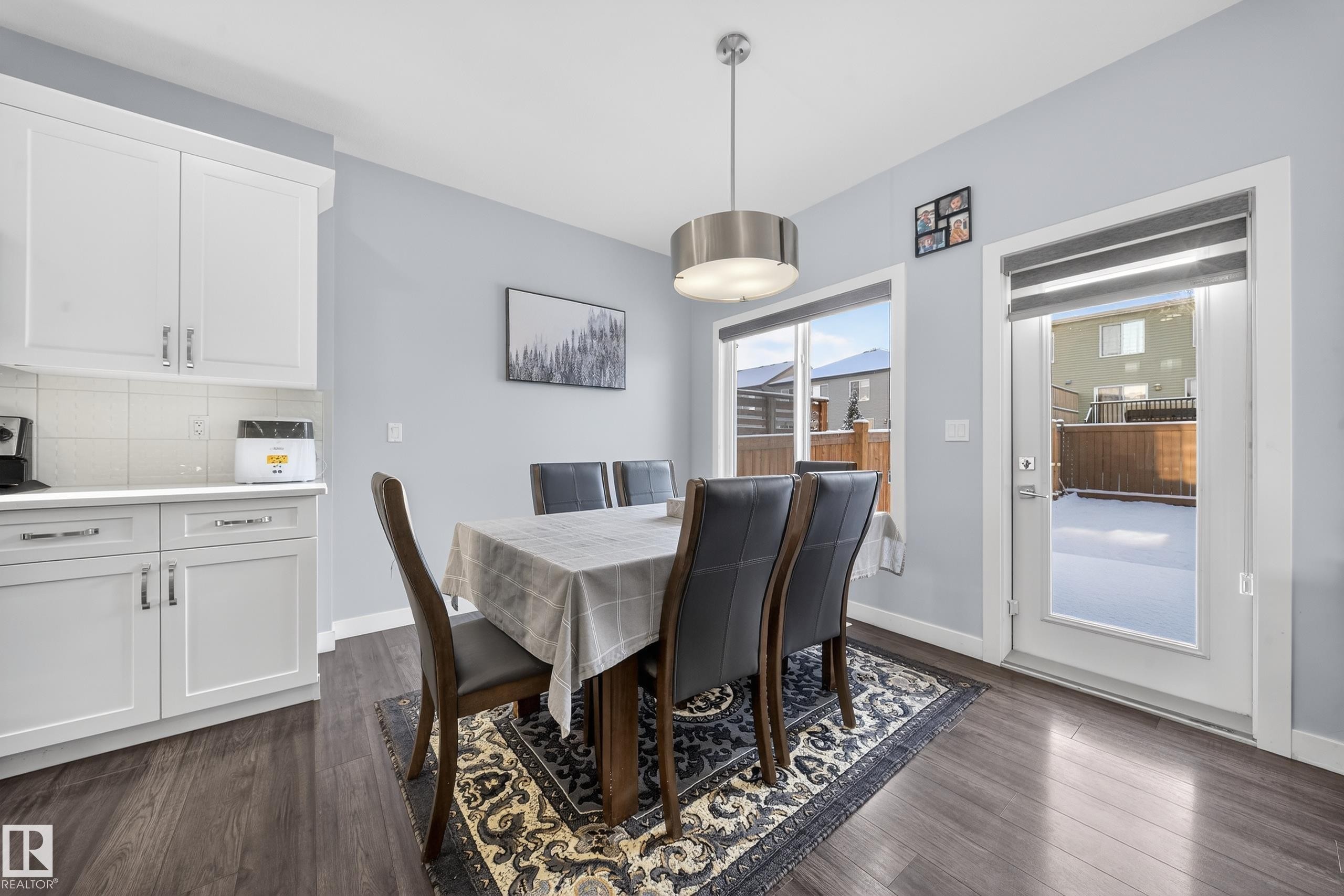 Dining area featuring wood-finish flooring, white cabinetry, a built-in countertop, a contemporary pendant light fixture, and a glass-paneled exterior door - 2084 Graydon Hill, Edmonton, AB
