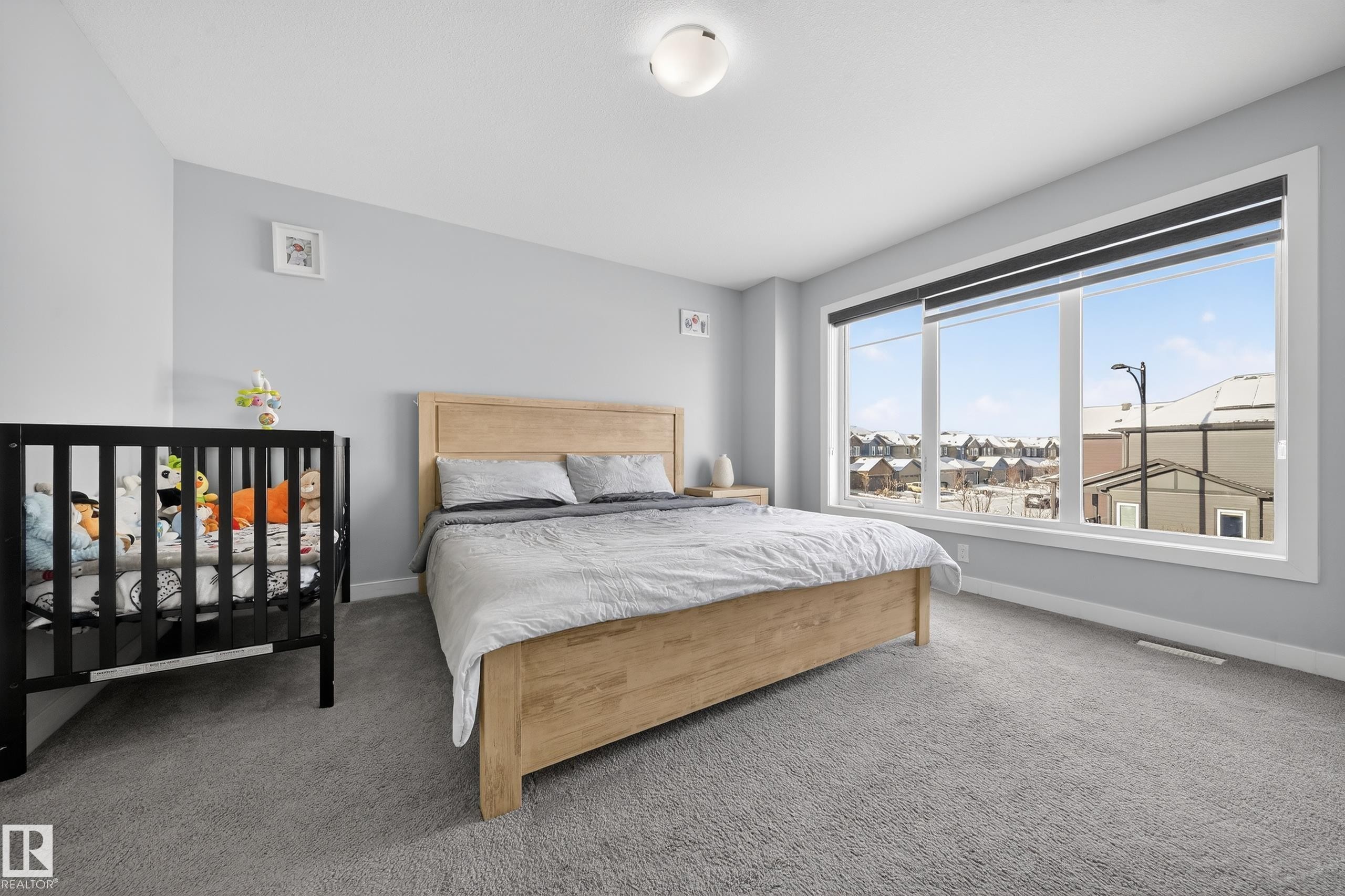 Light-filled bedroom featuring expansive windows with roller shades, light gray wall finishes, and gray carpeting - 2084 Graydon Hill, Edmonton, AB