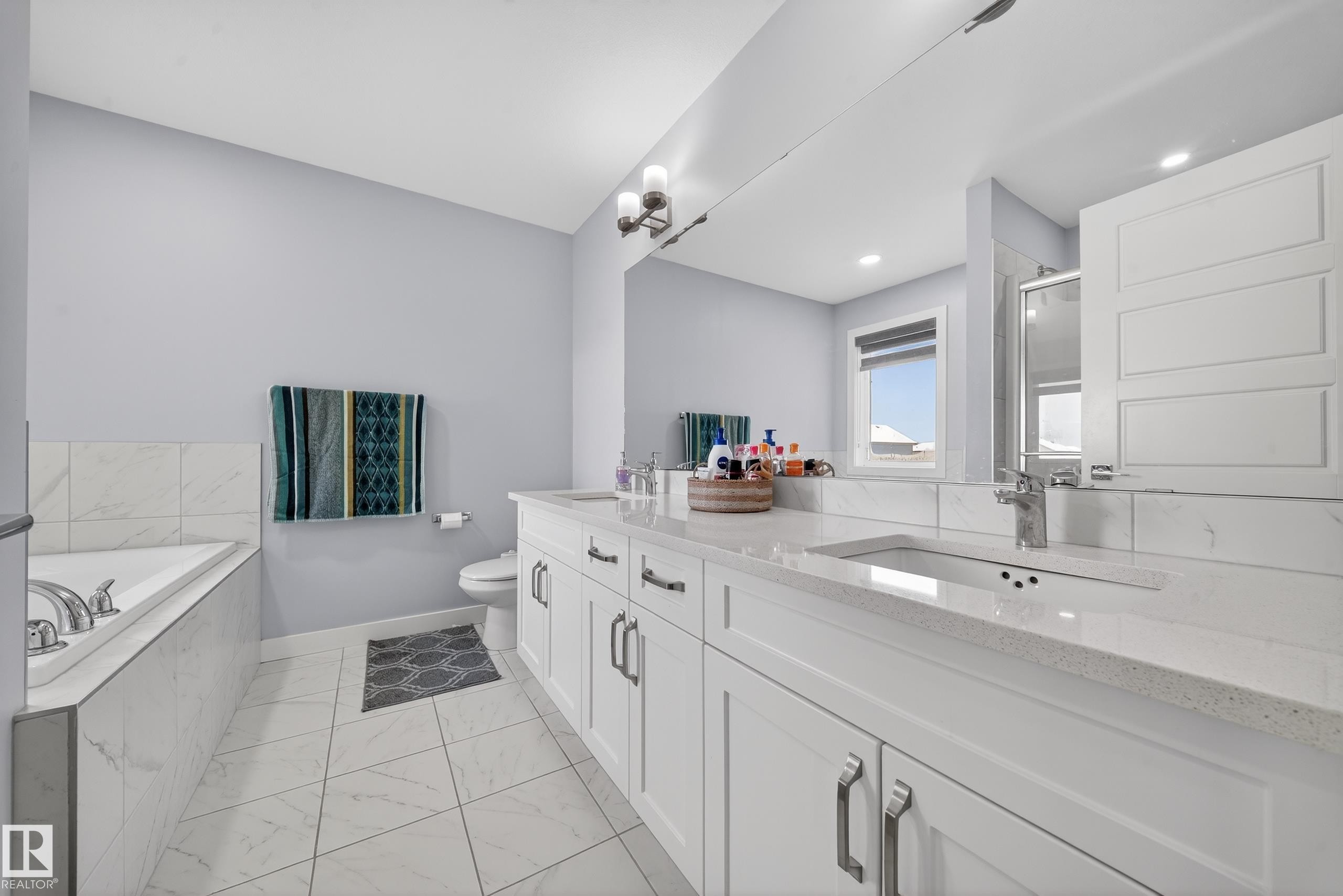 Bathroom featuring a dual vanity with white cabinetry and light-colored countertops, a built-in bathtub with tile surround, a built-in shower with glass enclosure, and light-colored tile flooring - 2084 Graydon Hill, Edmonton, AB