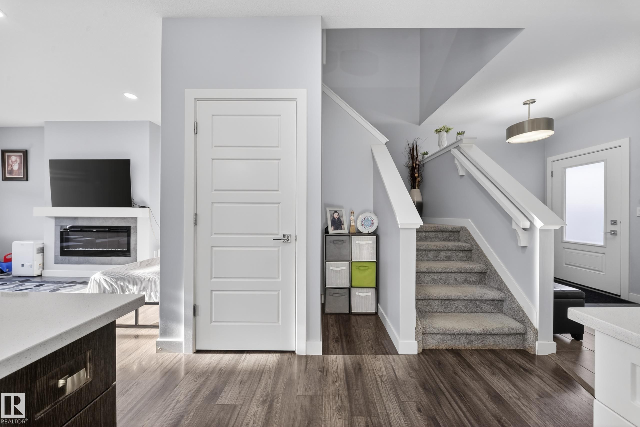 Open-concept interior featuring wood-finish flooring, a contemporary fireplace with mantel, white paneled doors, a carpeted staircase with white railings, and a front entry door with frosted glass - 2084 Graydon Hill, Edmonton, AB