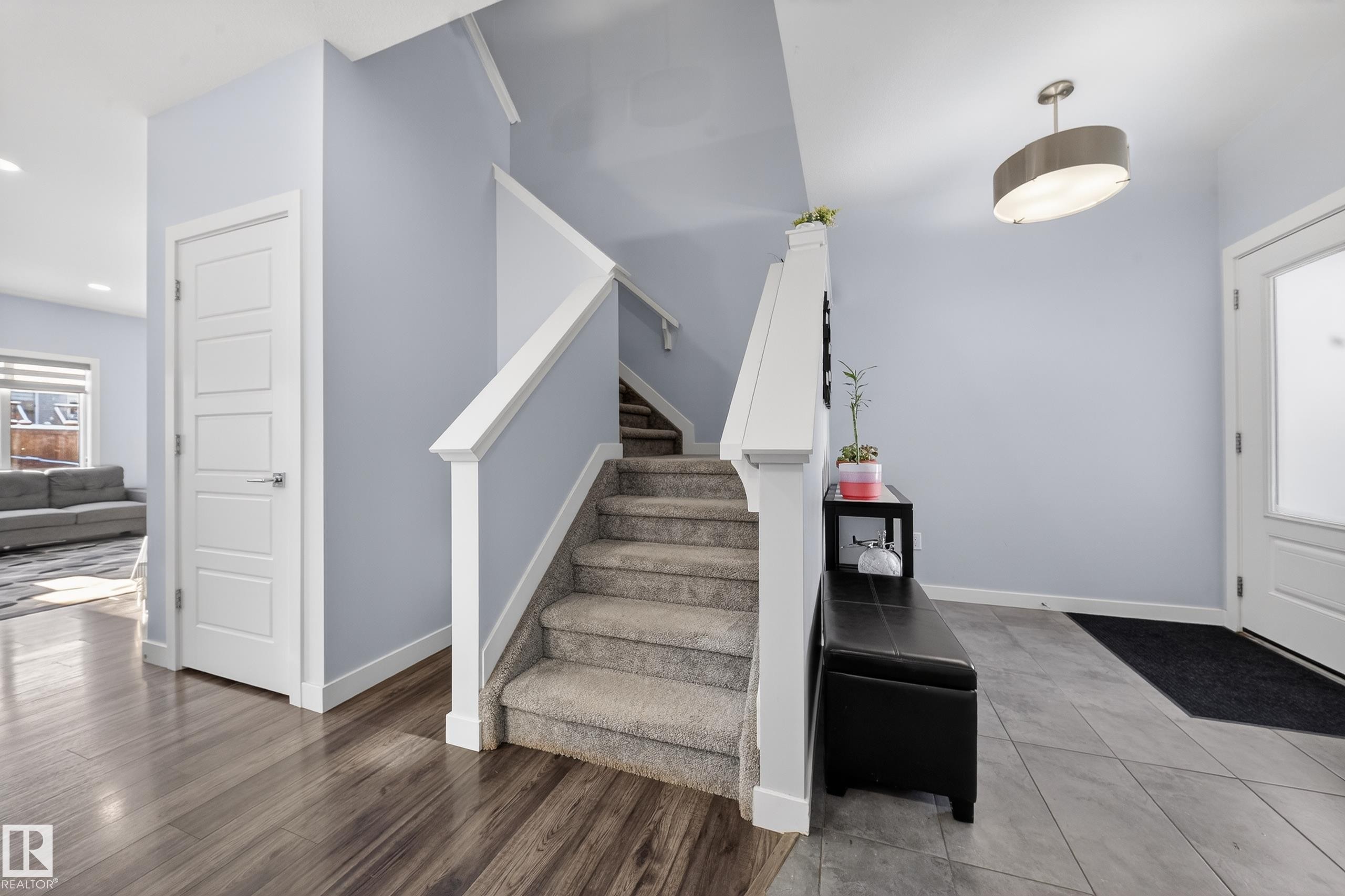 Inviting entryway featuring a carpeted staircase with white railings, wood-finish flooring, and light-toned wall paint - 2084 Graydon Hill, Edmonton, AB