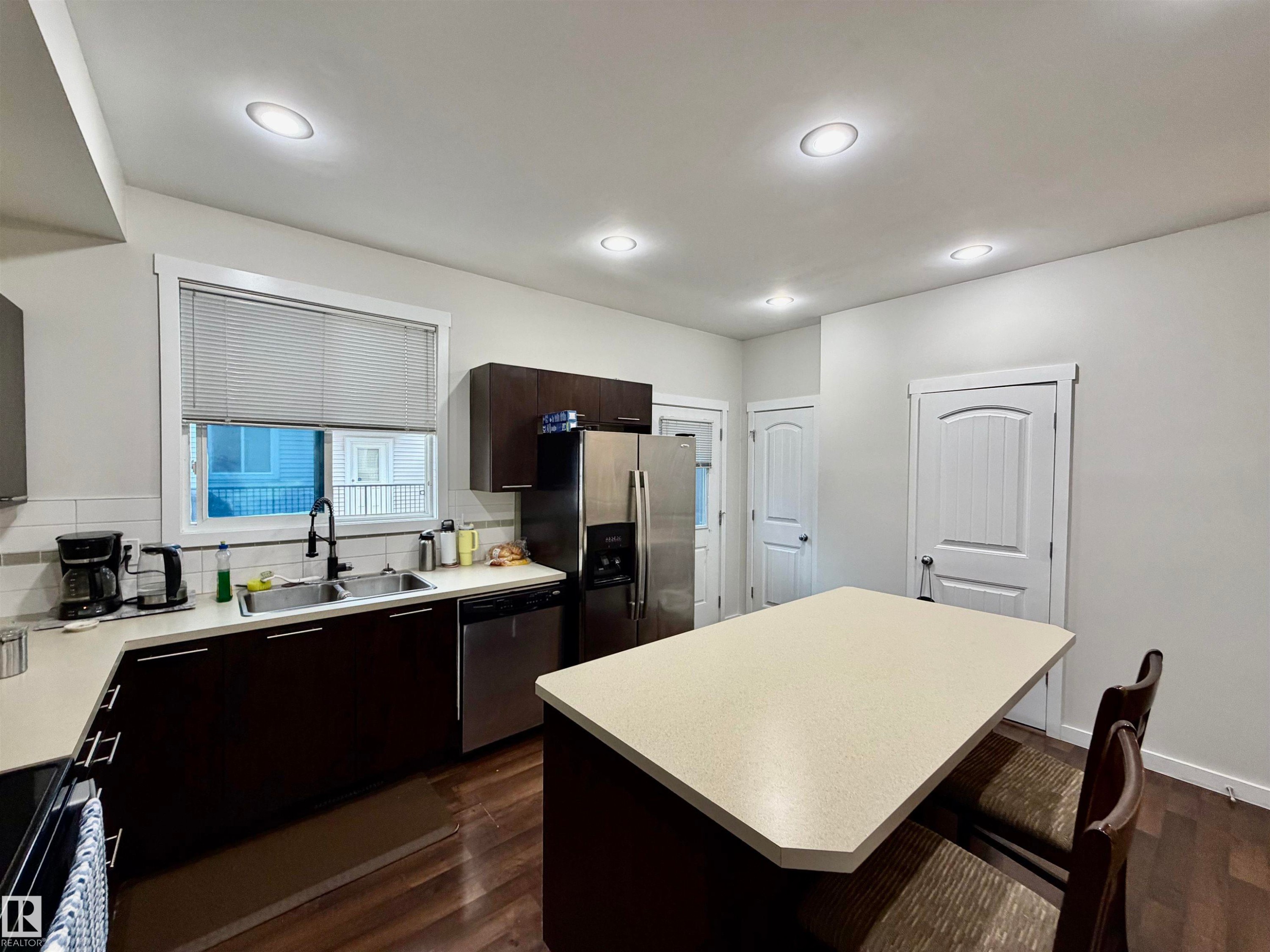 Kitchen featuring dark wood-finish cabinetry, stainless steel appliances, a double basin sink with a gooseneck faucet, light-toned countertops, and recessed lighting - 45 6075 Schonsee Way, Edmonton, AB