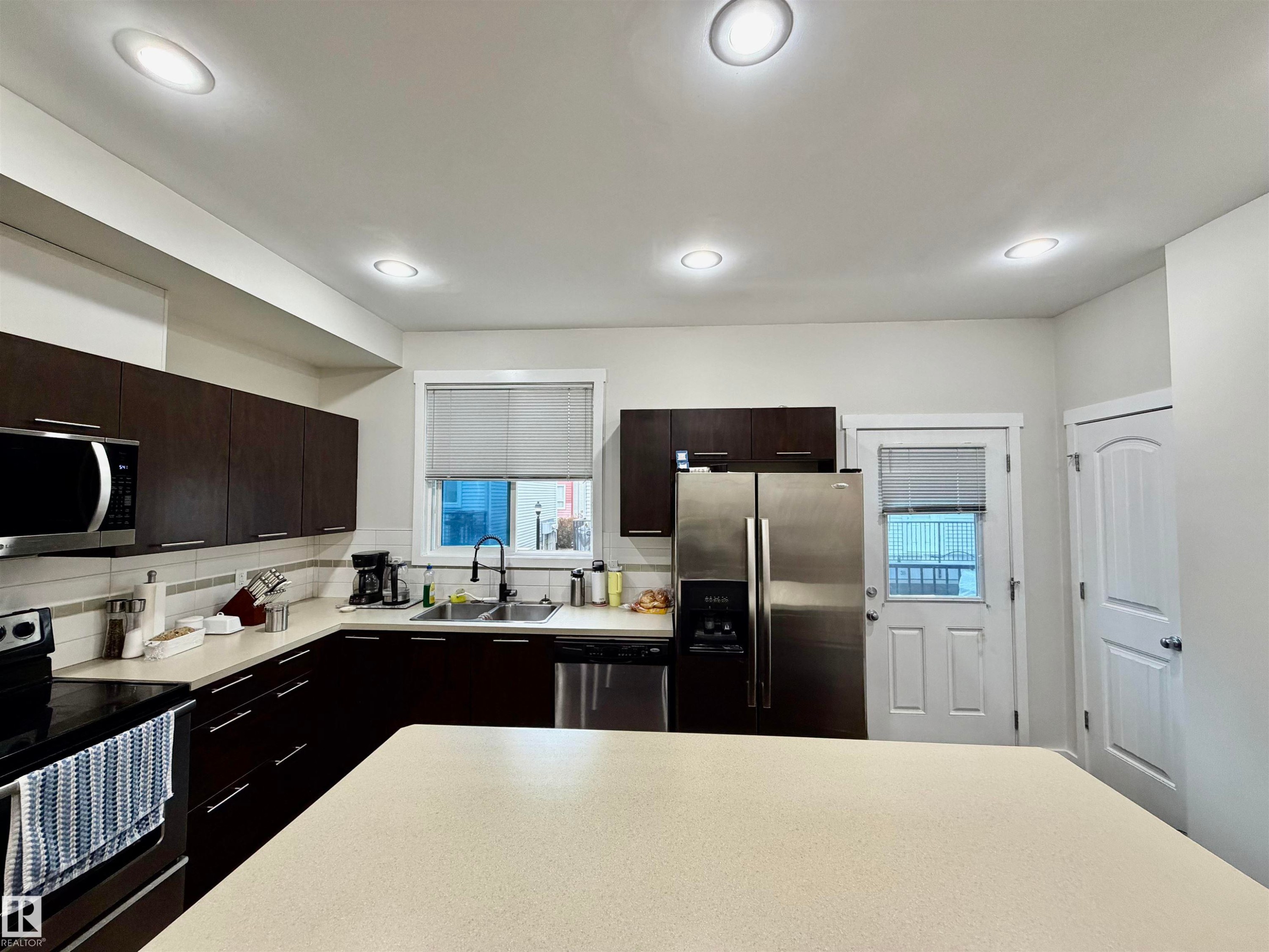 Kitchen featuring dark wood-finish cabinetry, stainless steel appliances, recessed lighting, and a light-toned countertop - 45 6075 Schonsee Way, Edmonton, AB