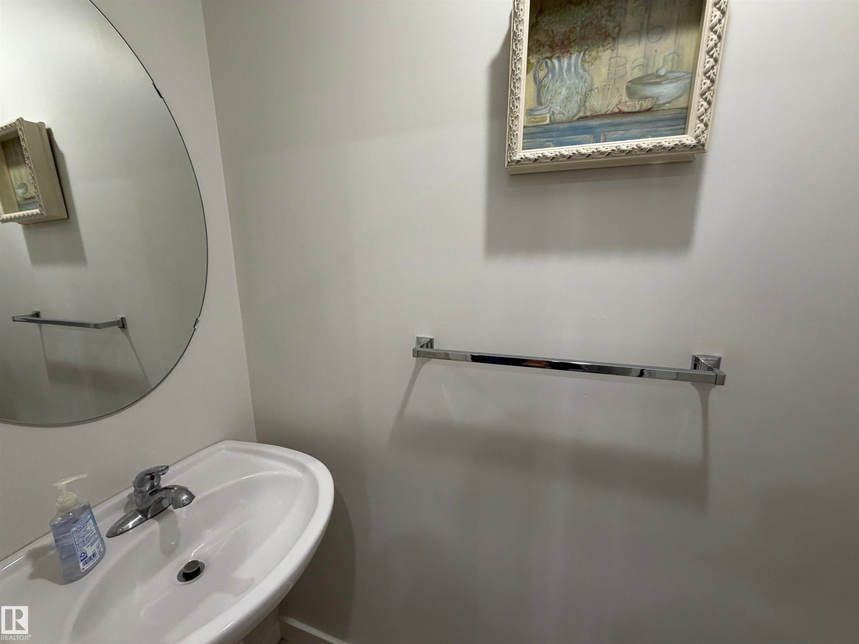 Pedestal sink with chrome faucet, complemented by a large circular frameless mirror - 45 6075 Schonsee Way, Edmonton, AB