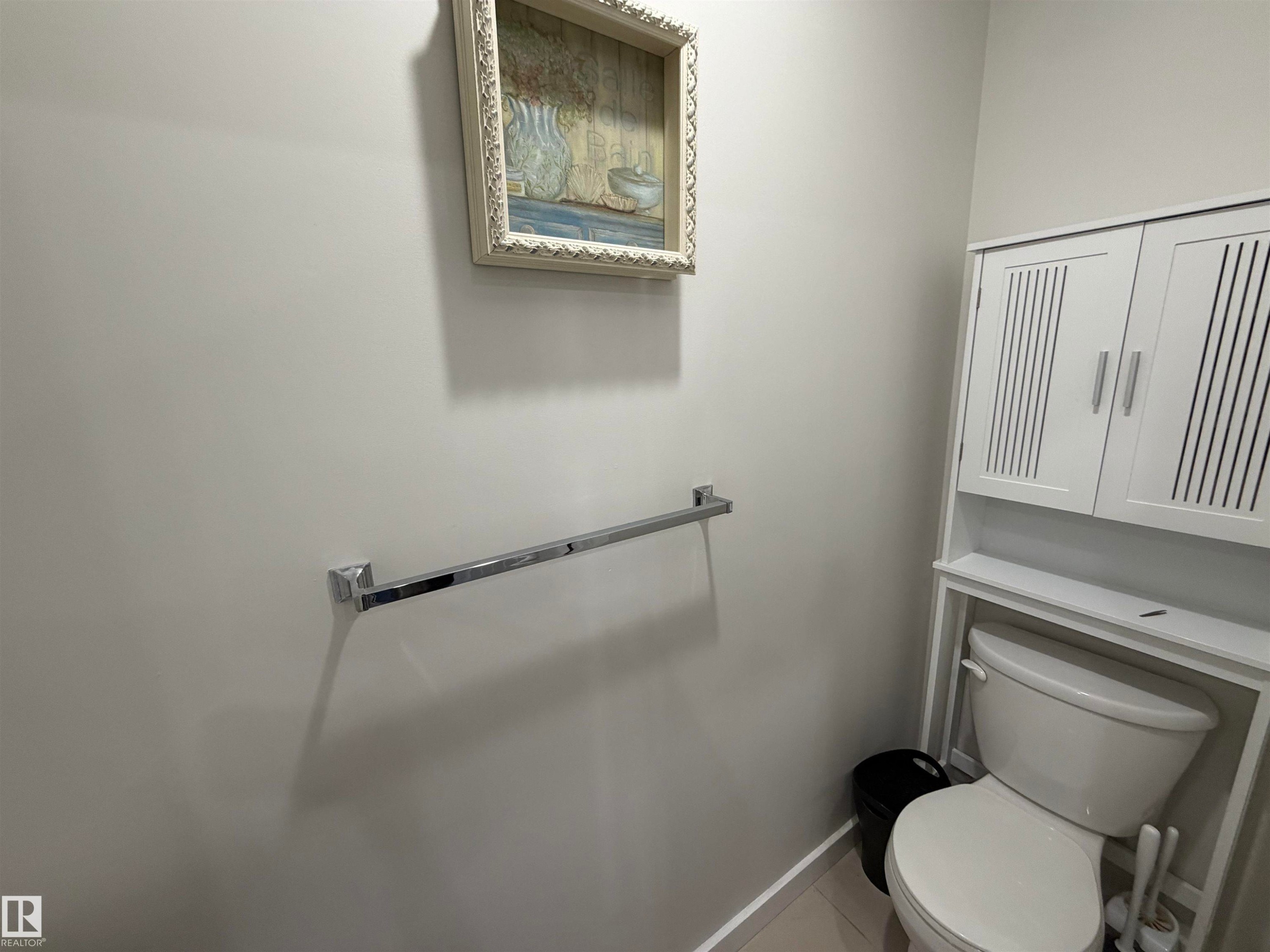 Bathroom featuring a white toilet, chrome towel bar, and white wall-mounted storage cabinet with slatted doors - 45 6075 Schonsee Way, Edmonton, AB