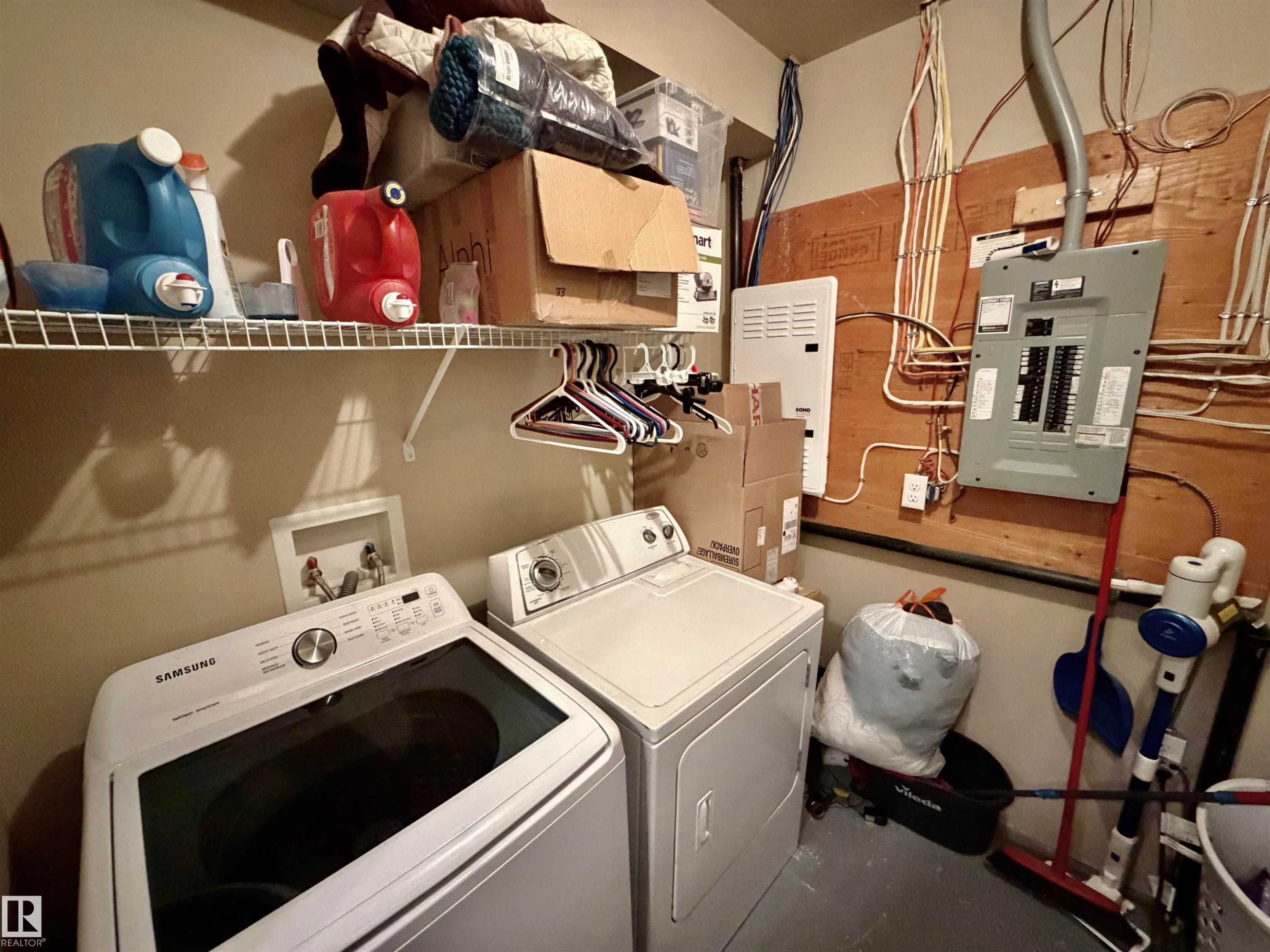 Dedicated laundry area featuring a washer and dryer hookup, overhead wire shelving, and a visible electrical panel - 45 6075 Schonsee Way, Edmonton, AB