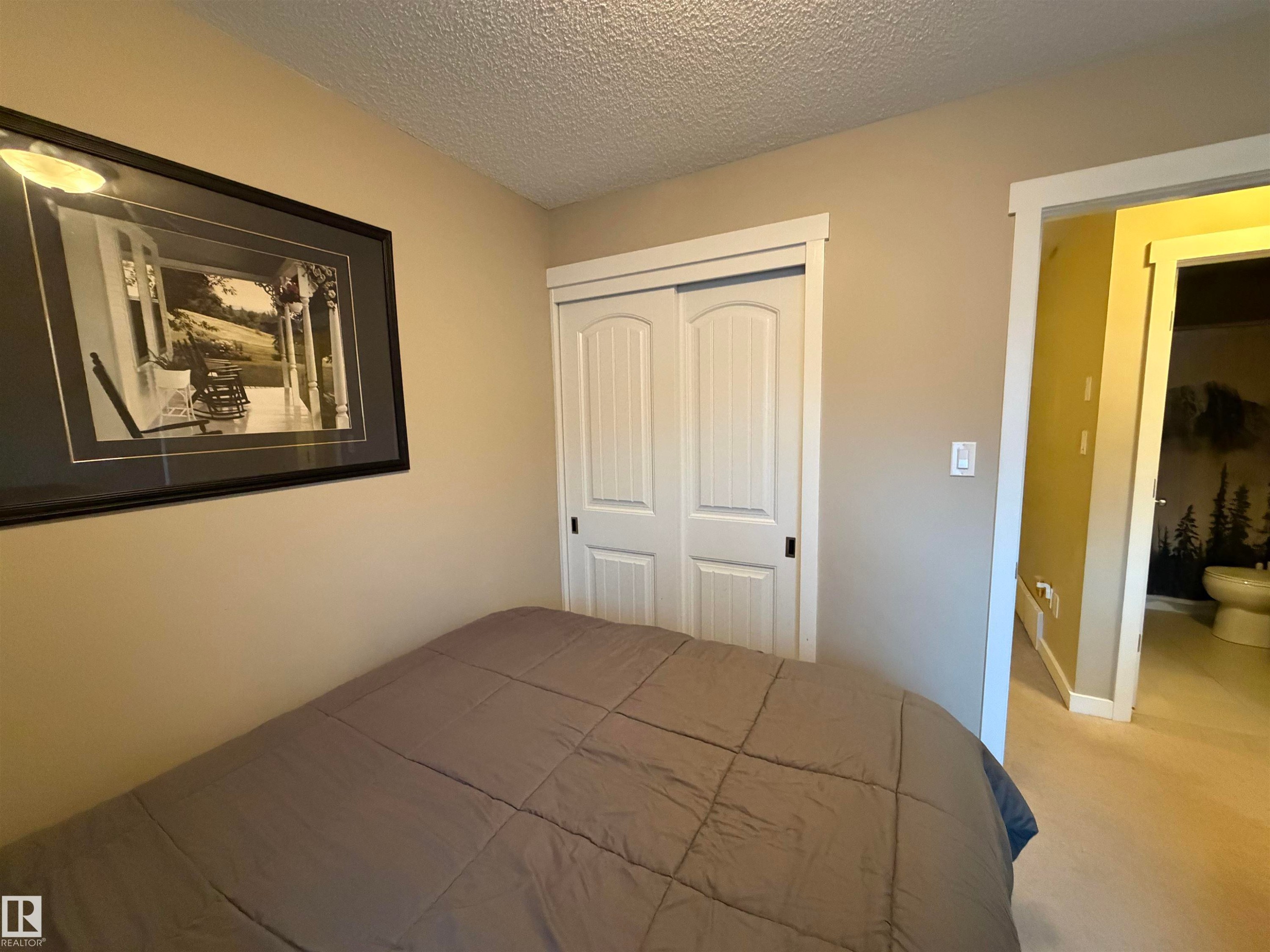 Neutral-toned room featuring a textured ceiling, a built-in closet with white panel doors, and a doorway to a separate space with a toilet - 45 6075 Schonsee Way, Edmonton, AB