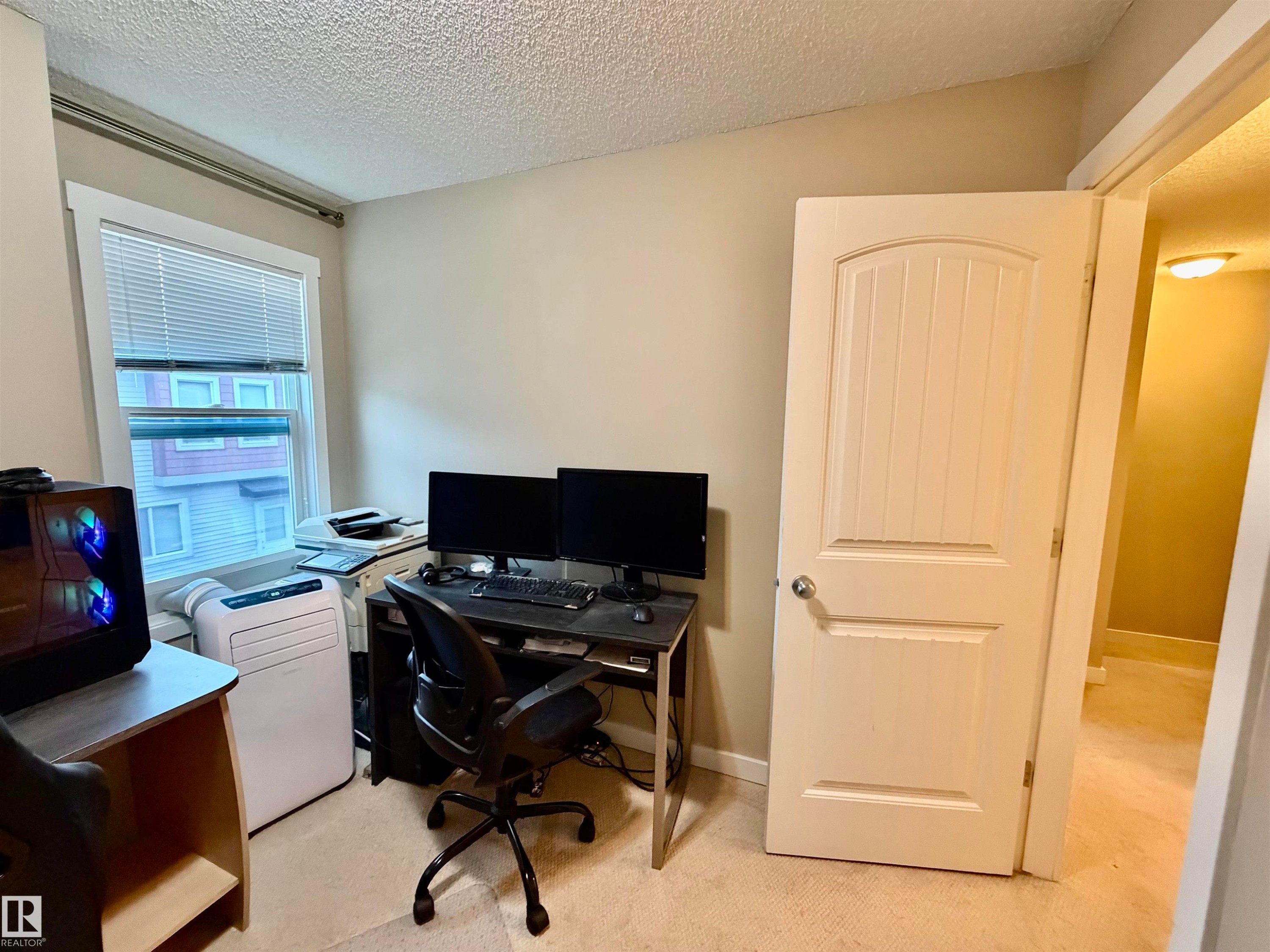 Carpeted room with a single window featuring white blinds and trim, a textured ceiling, and neutral-toned walls - 45 6075 Schonsee Way, Edmonton, AB