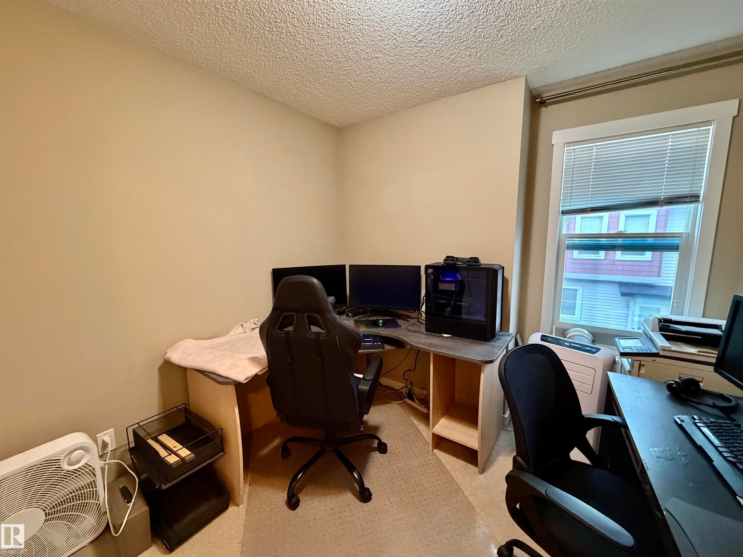 Versatile room featuring a window with white blinds, neutral wall paint, and textured ceiling - 45 6075 Schonsee Way, Edmonton, AB