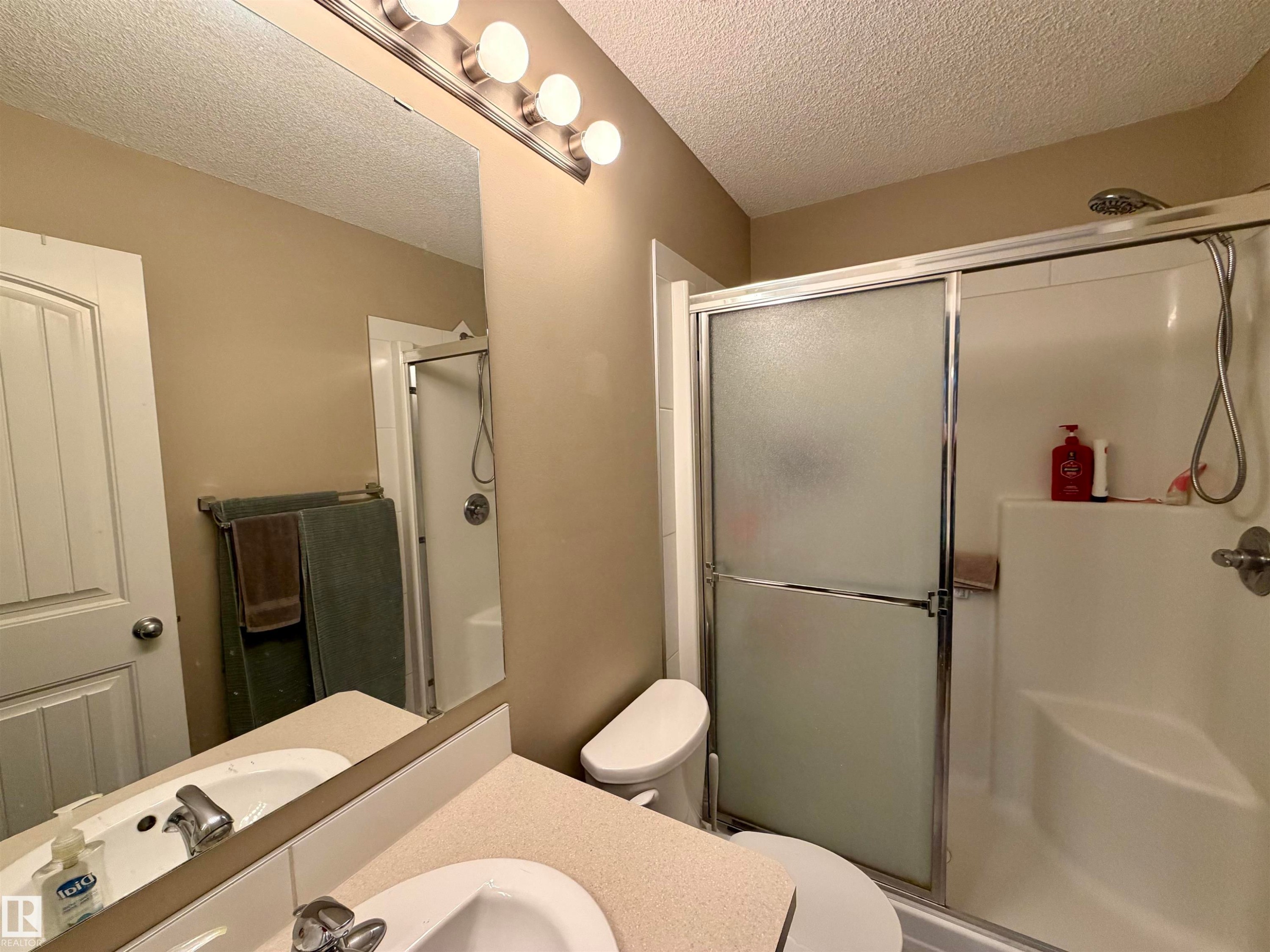 Three-light vanity fixture above a large mirror and a shower with frosted sliding glass doors - 45 6075 Schonsee Way, Edmonton, AB