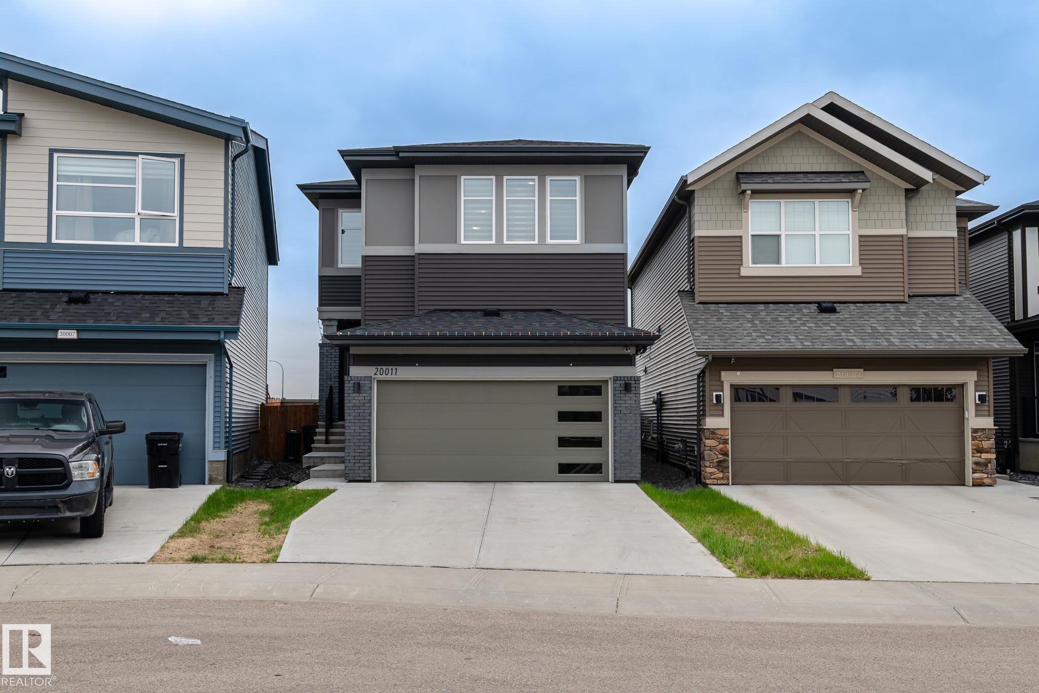Contemporary two-story exterior featuring a multi-tone facade, white window trim, and an attached two-car garage with horizontal paneling and frosted glass inserts - 20011 26, Edmonton, AB