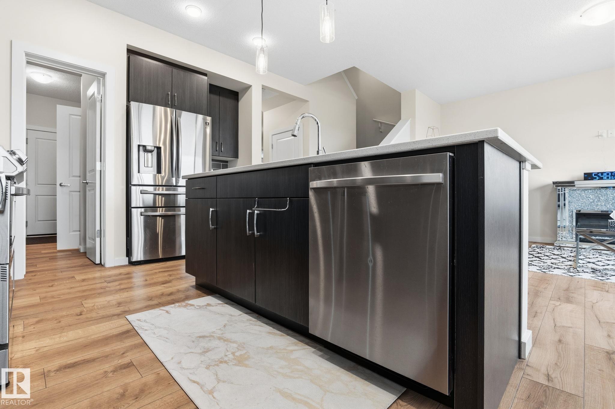 Kitchen featuring an island with a light-toned countertop, dark wood-finish cabinetry, and a stainless steel dishwasher - 20011 26, Edmonton, AB