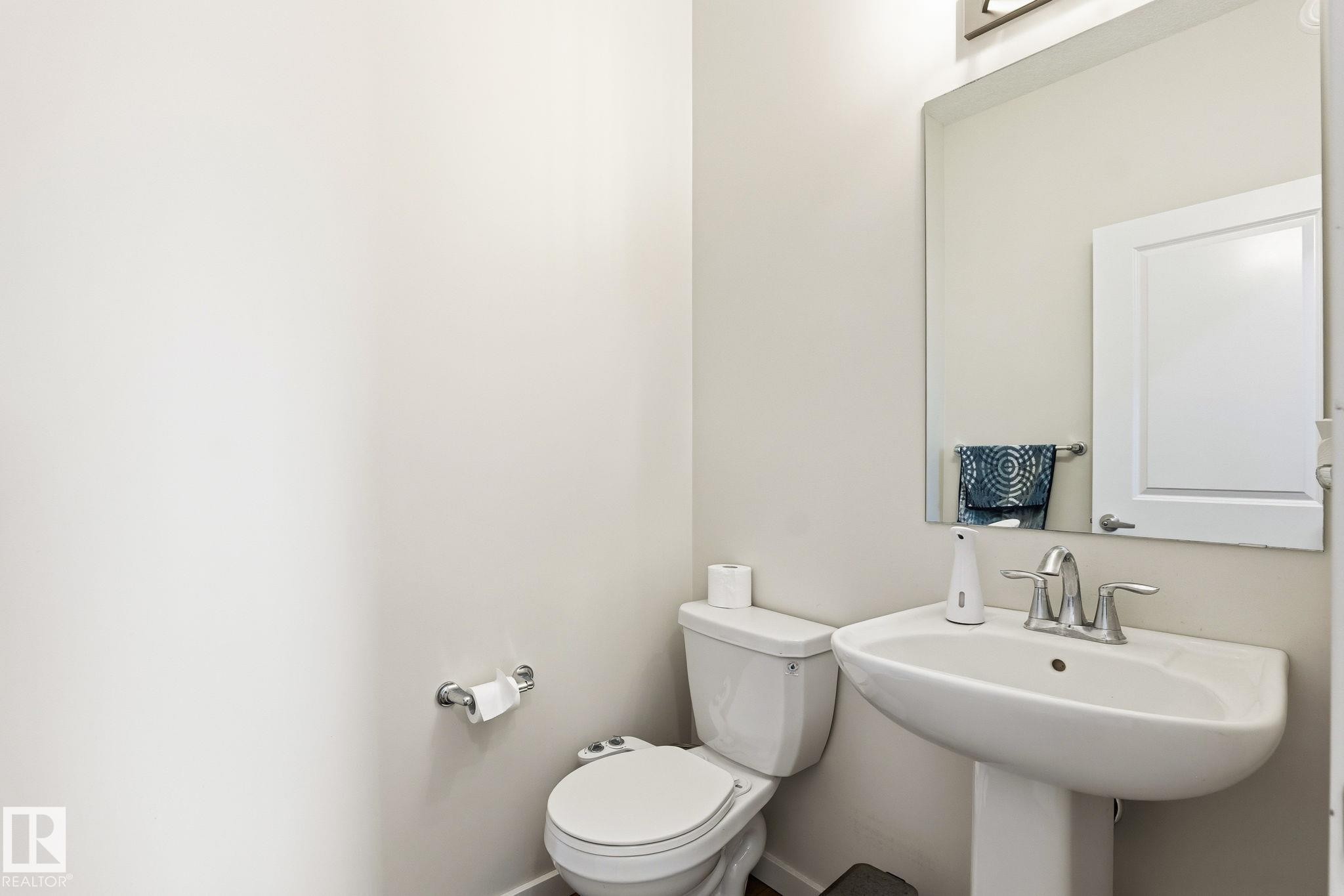 Pedestal sink with chrome faucet, a rectangular wall-mounted mirror, and a modern toilet - 20011 26, Edmonton, AB