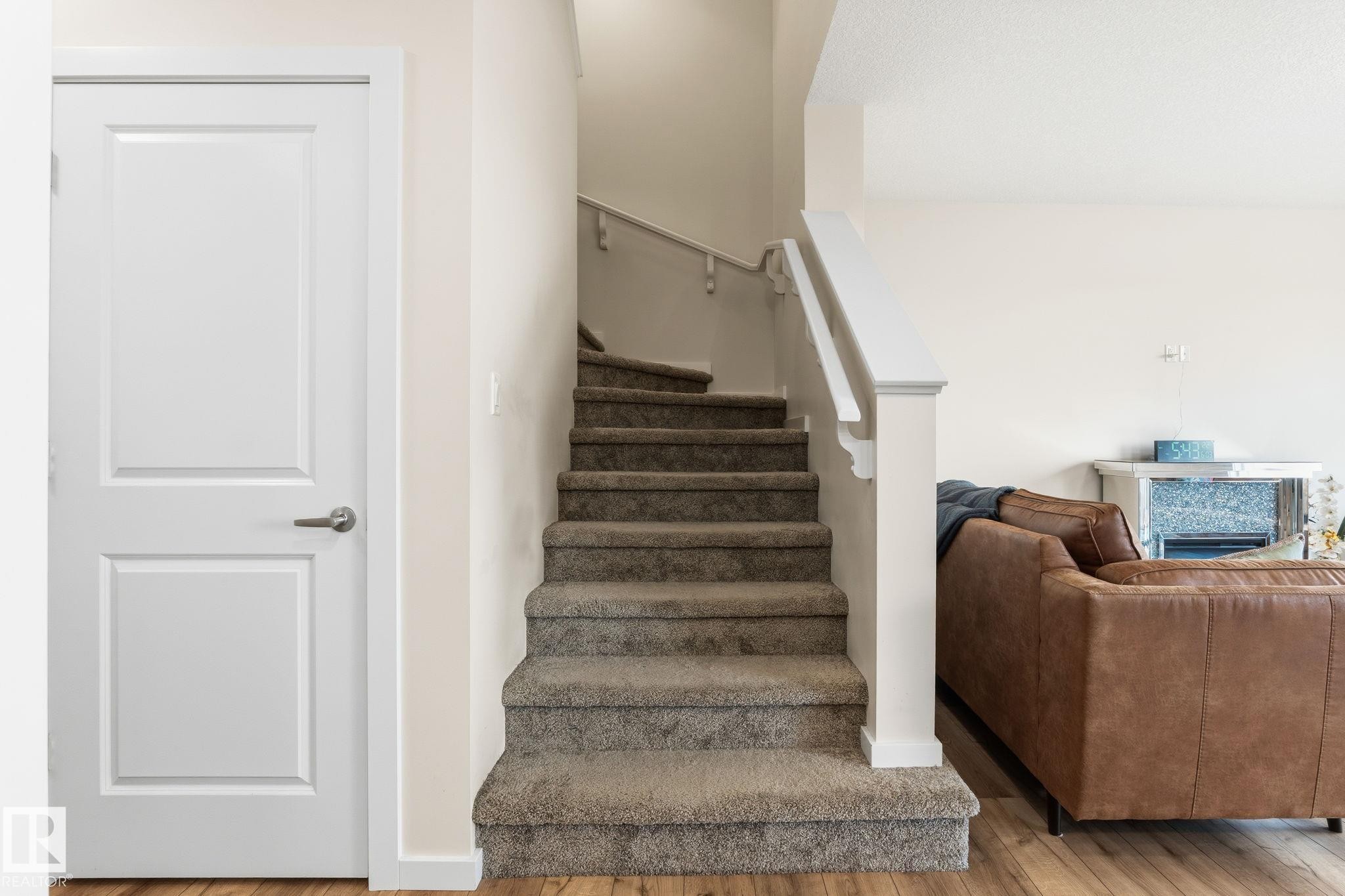 Carpeted staircase with white railing, wood-finish flooring, and a paneled interior door - 20011 26, Edmonton, AB