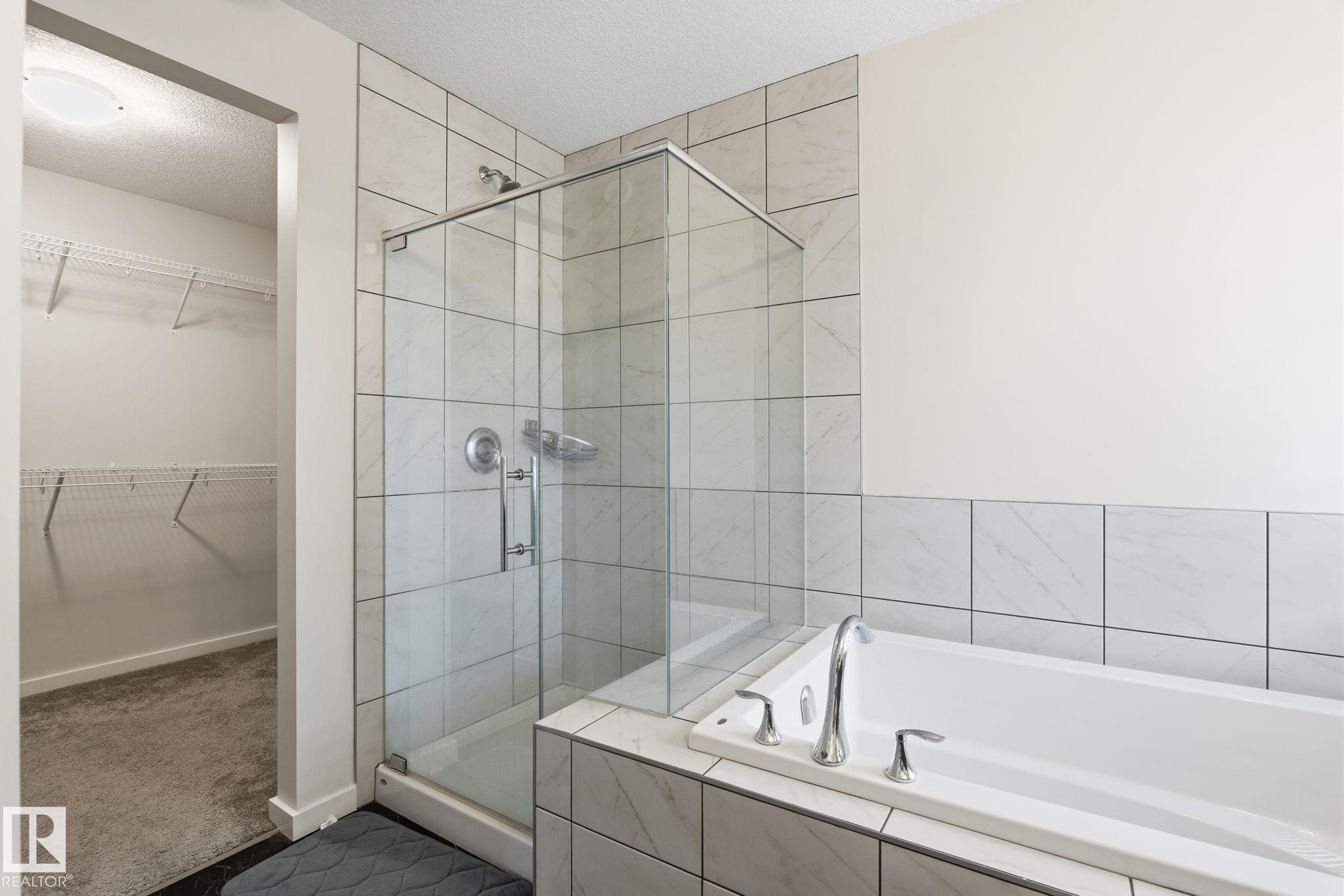 Shower with glass enclosure and light-toned tile surround, freestanding tub with chrome fixtures, and an adjacent walk-in closet with wire shelving - 20011 26, Edmonton, AB