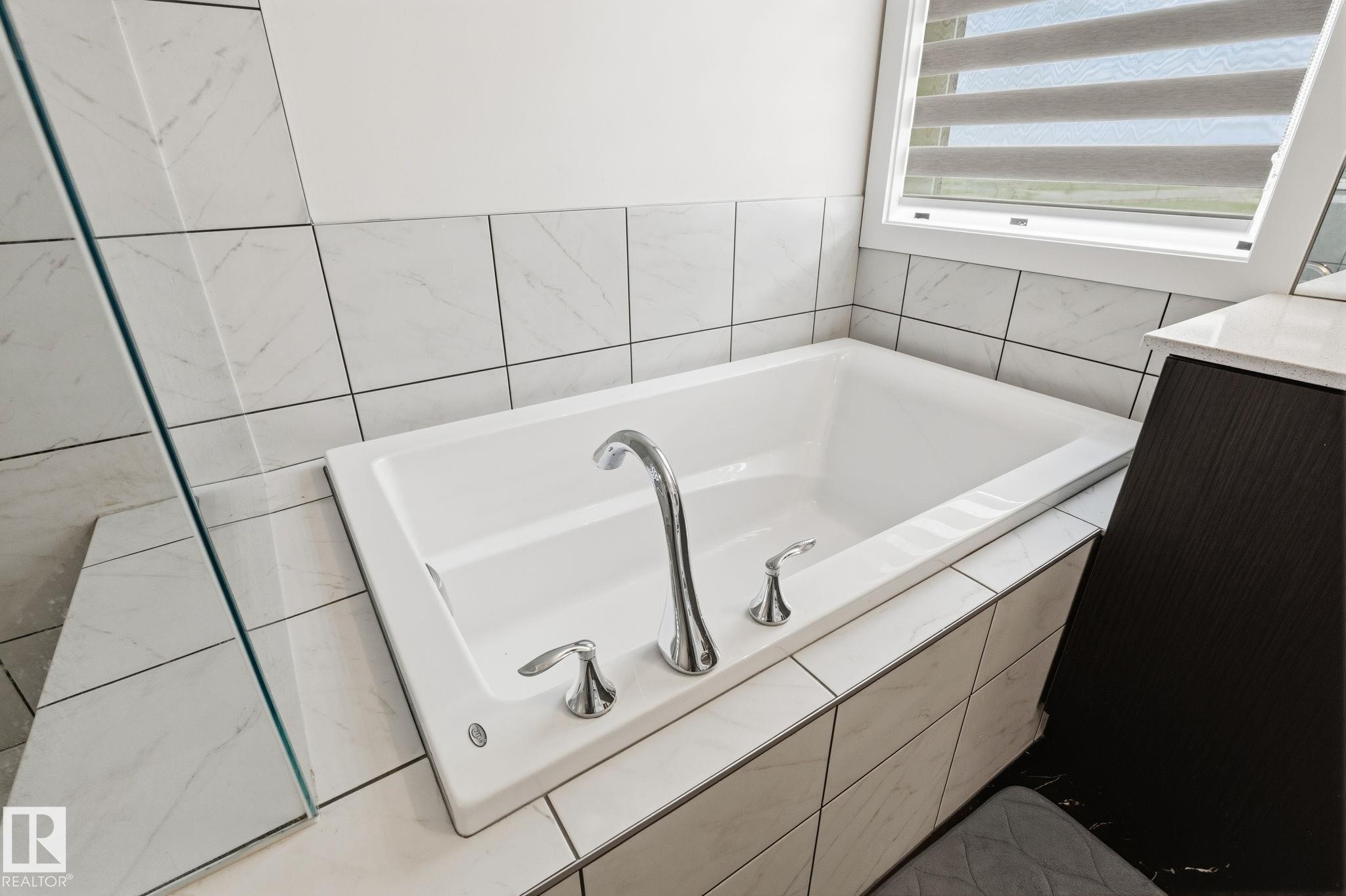Built-in soaking tub with chrome fixtures, surrounded by white rectangular wall tiles - 20011 26, Edmonton, AB