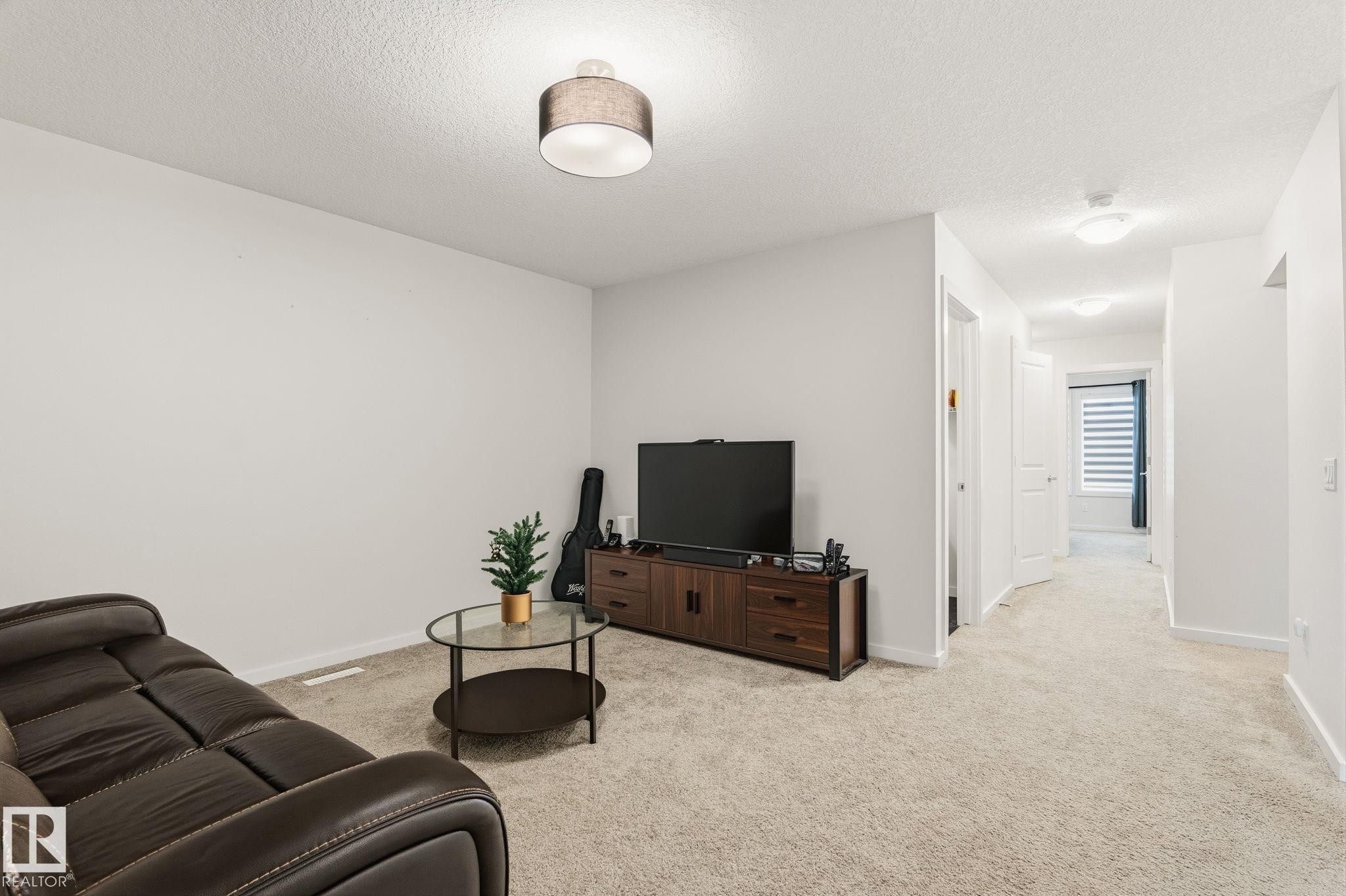Spacious carpeted room featuring light gray walls and recessed lighting, with a hallway extending from the right - 20011 26, Edmonton, AB