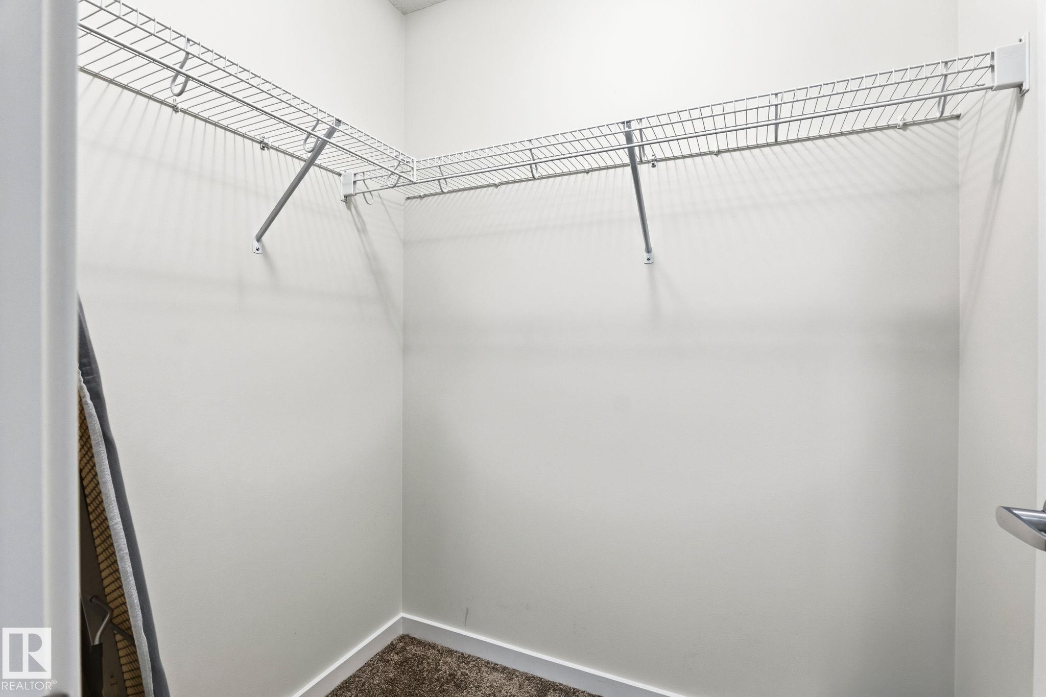 Walk-in closet featuring wire shelving, wire hanging rods, light gray wall paint, and short-pile carpet - 20011 26, Edmonton, AB