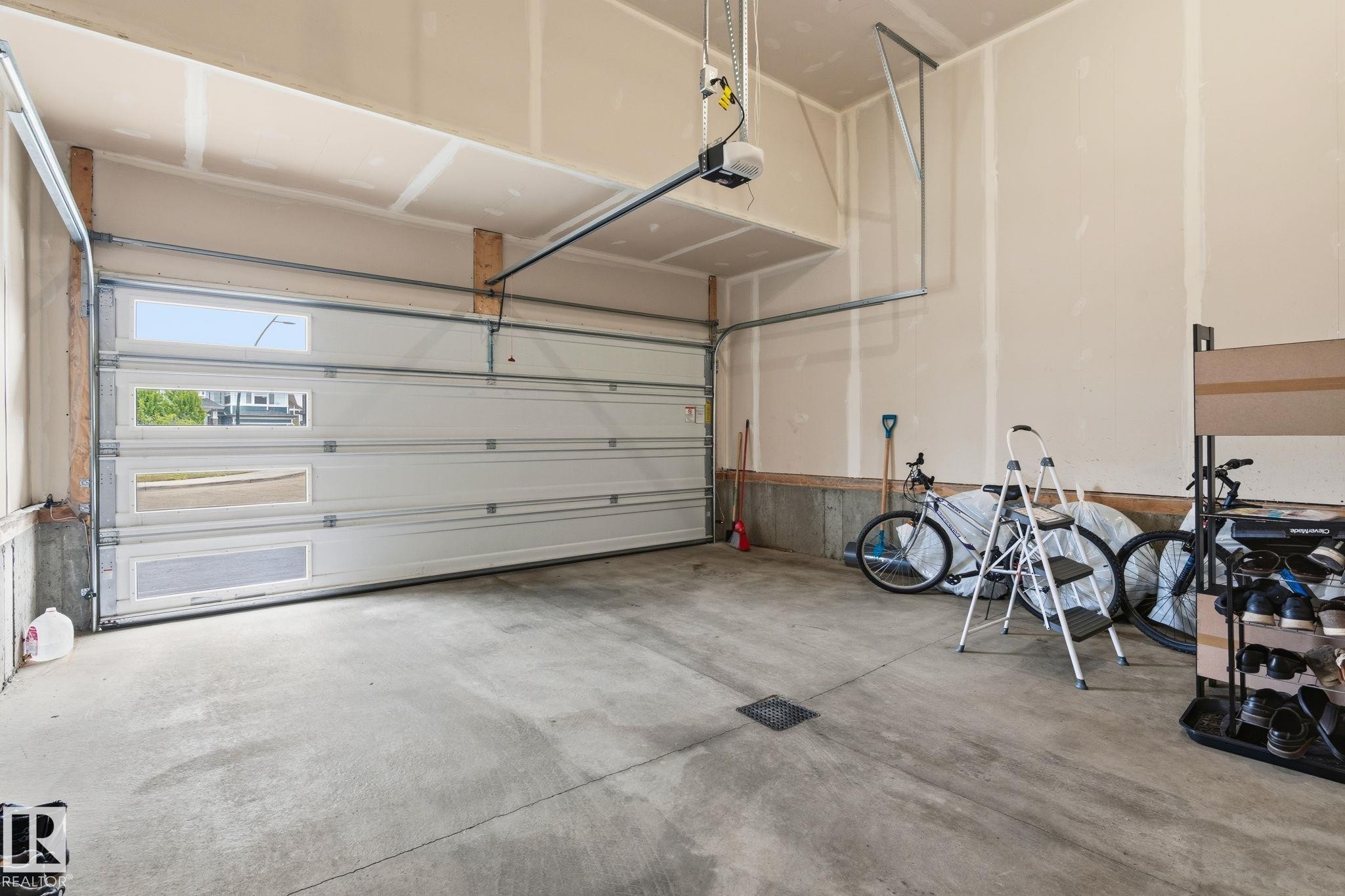 Spacious garage featuring a sectional overhead door with upper and middle rectangular window inserts, a concrete floor, and an automatic garage door opener - 20011 26, Edmonton, AB