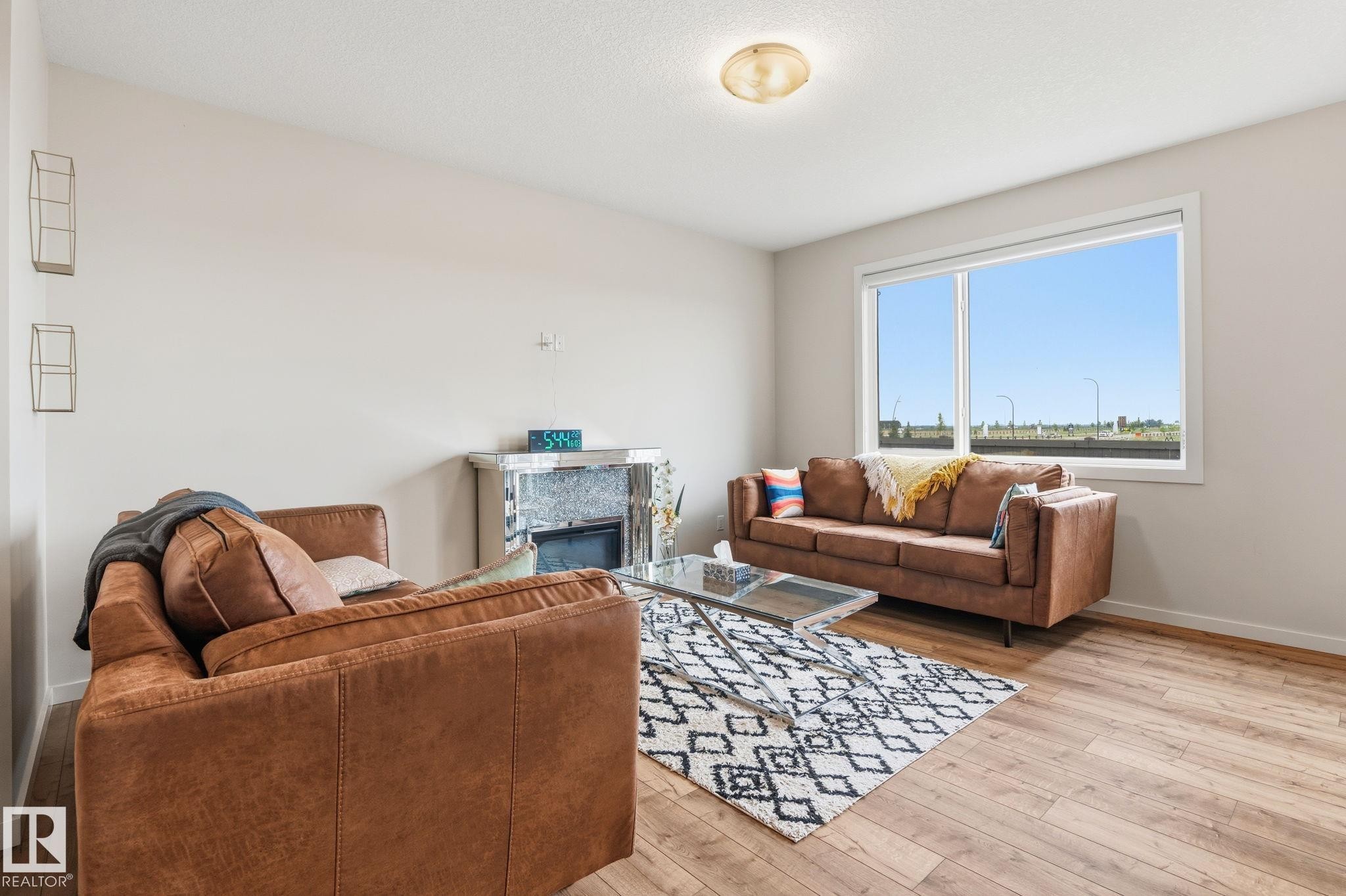 Living area featuring wood-finish flooring, a large window, a ceiling-mounted light fixture, and light-colored walls - 20011 26, Edmonton, AB