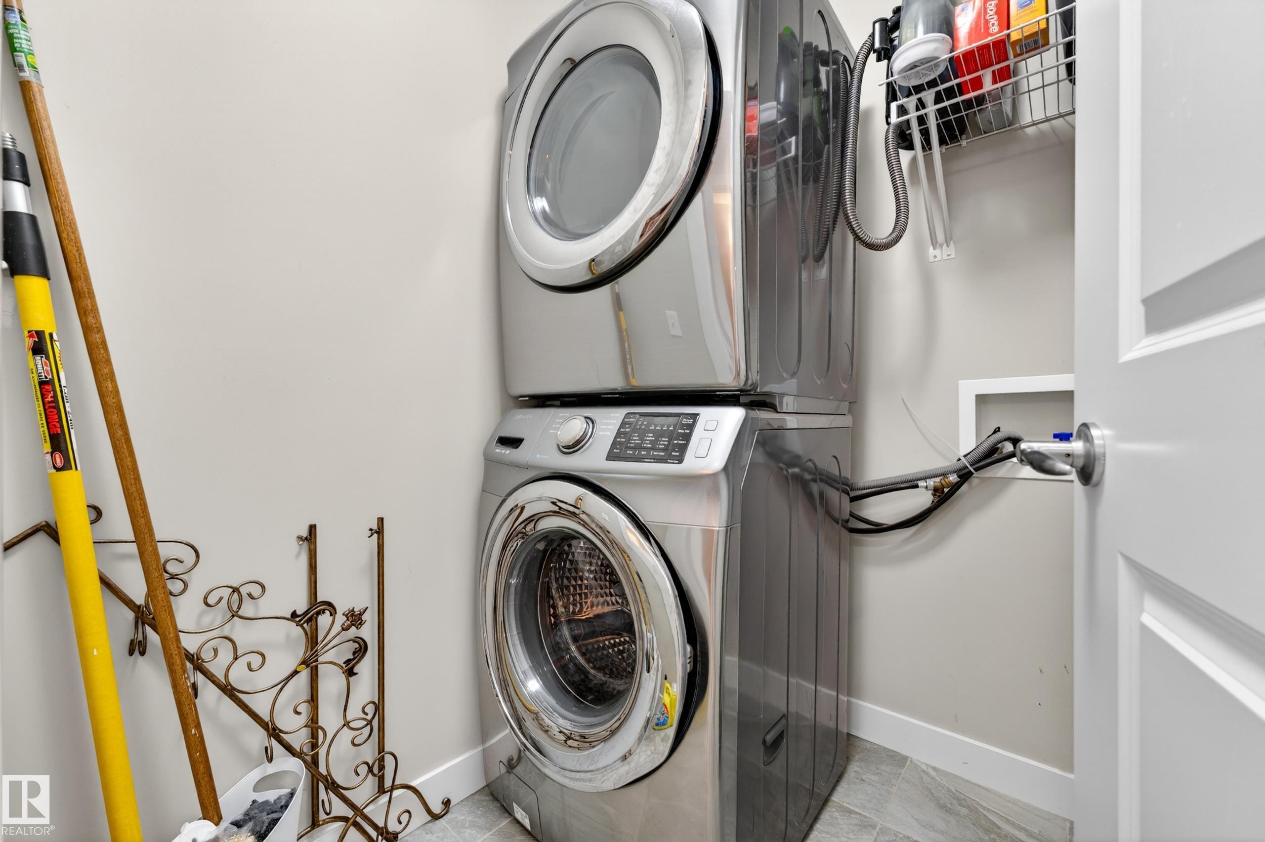 Dedicated laundry area featuring stacked front-load appliances, a wall-mounted wire shelf, and light gray wall paint - 85 165 Cy Becker Boulevard, Edmonton, AB - Indoor Photo Showing Laundry Room