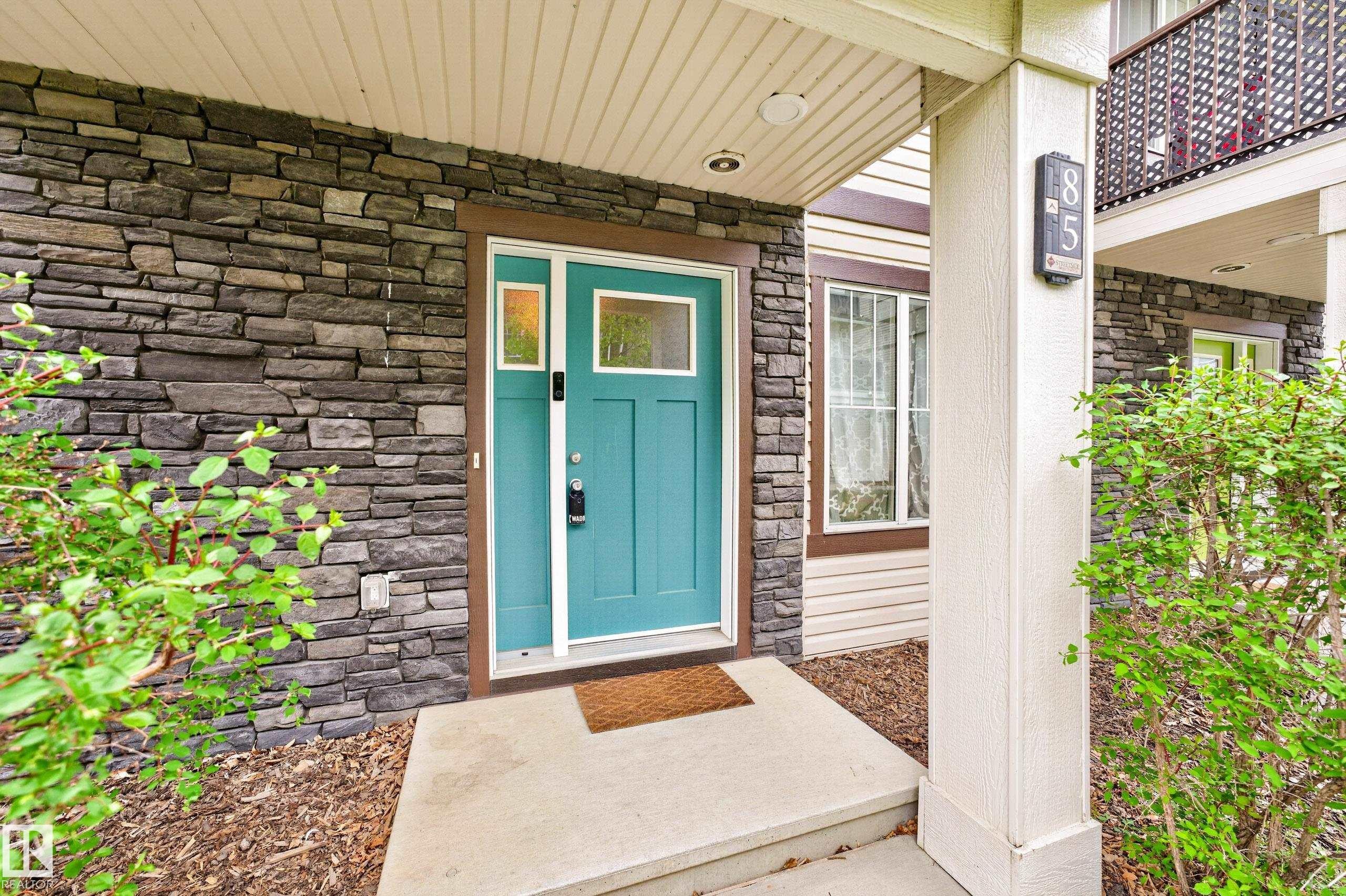 Entryway featuring a vibrant teal front door with transom windows, dark stacked stone facade, and a concrete landing - 85 165 Cy Becker Boulevard, Edmonton, AB - Outdoor