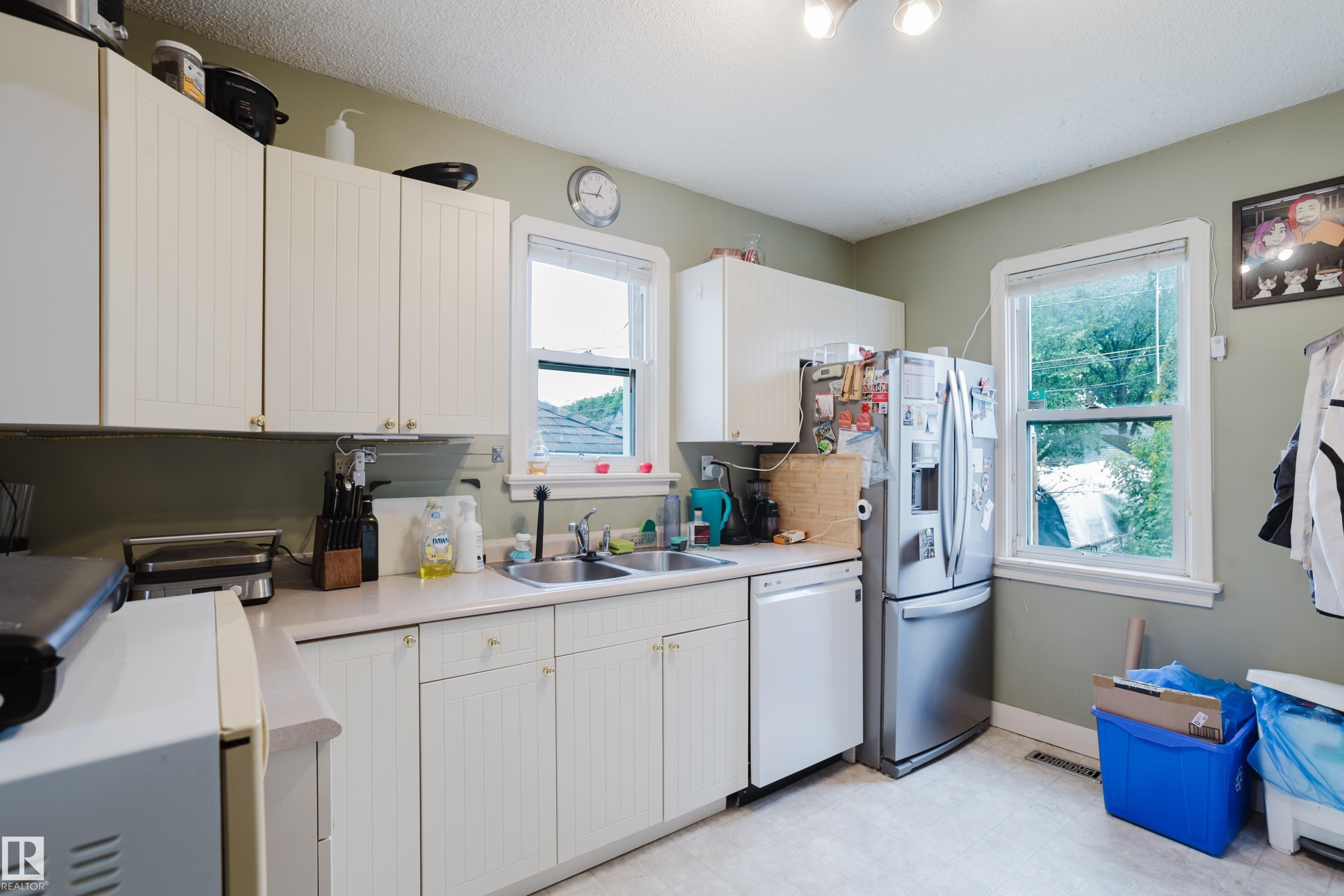 Kitchen featuring white paneled cabinetry, light countertops, and a dual-basin stainless steel sink - 11158 65 Street, Edmonton, AB
