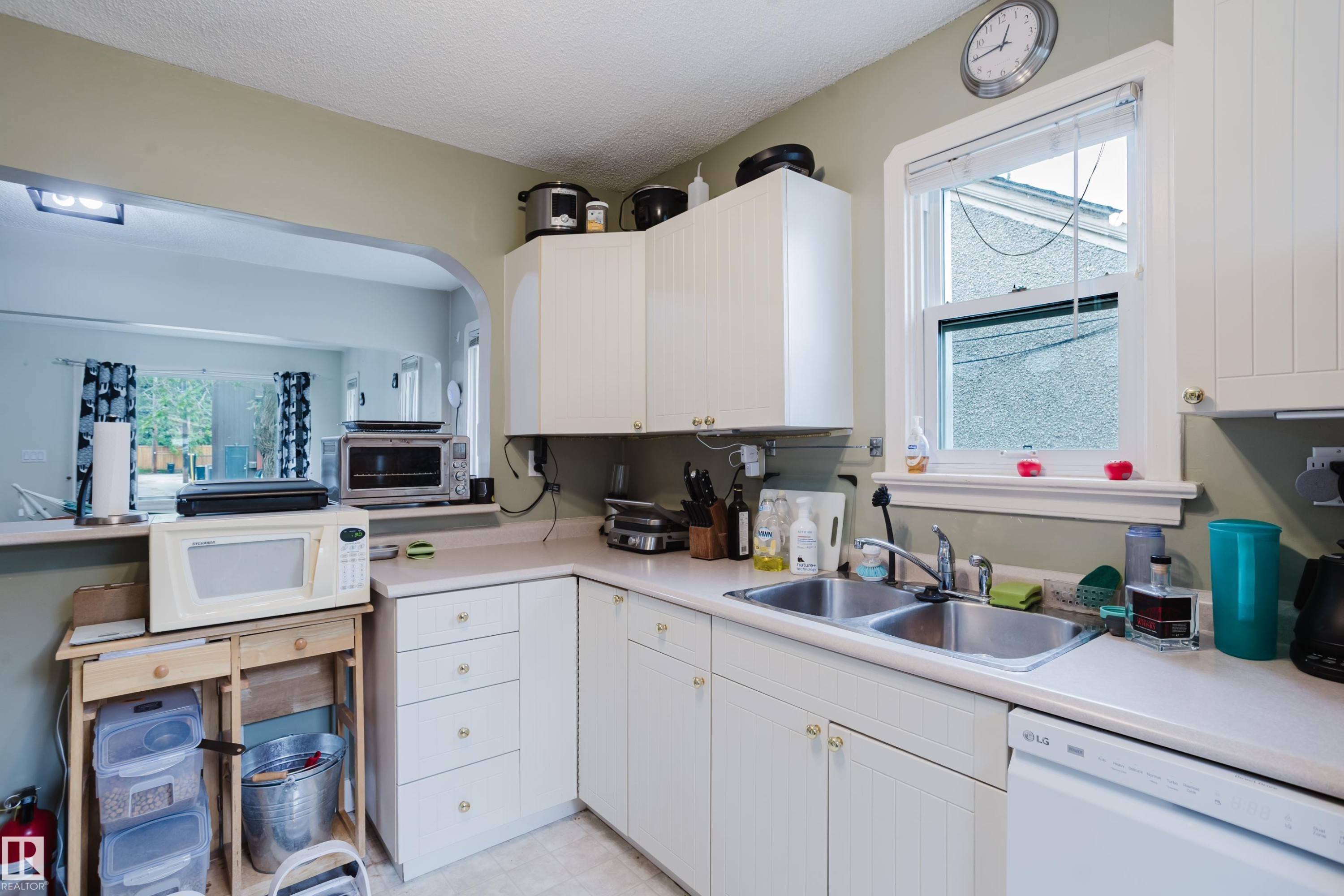 Kitchen featuring white cabinetry, a double basin stainless steel sink, a window over the sink, and an arched pass-through to an adjacent room - 11158 65 Street, Edmonton, AB