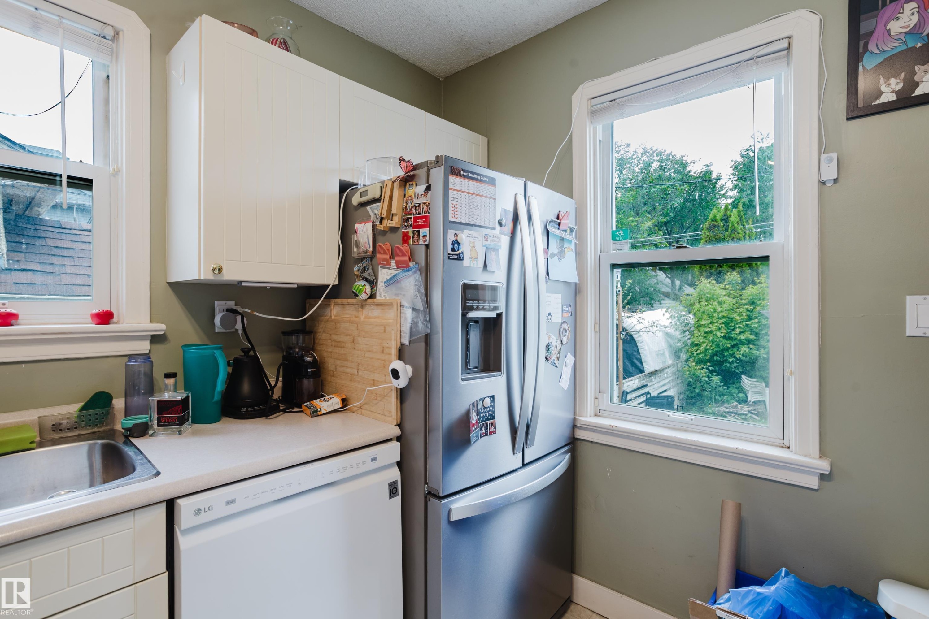 Kitchen area featuring white cabinetry, a stainless steel refrigerator, white countertops, and a stainless steel sink - 11158 65 Street, Edmonton, AB