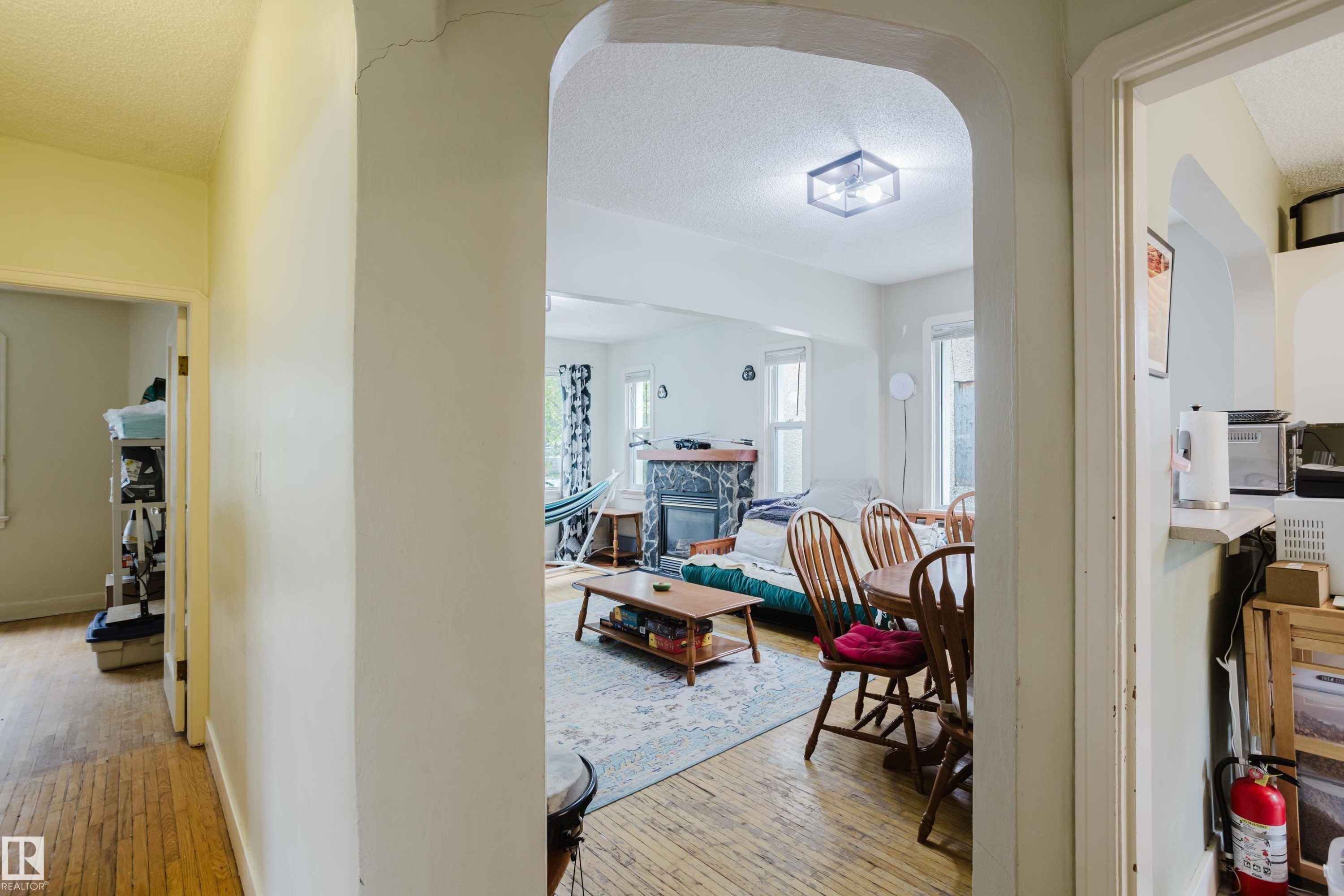 Arched entryway opening to a living area featuring wood-finish flooring, a decorative fireplace with stone surround, and an overhead flush-mount light fixture - 11158 65 Street, Edmonton, AB