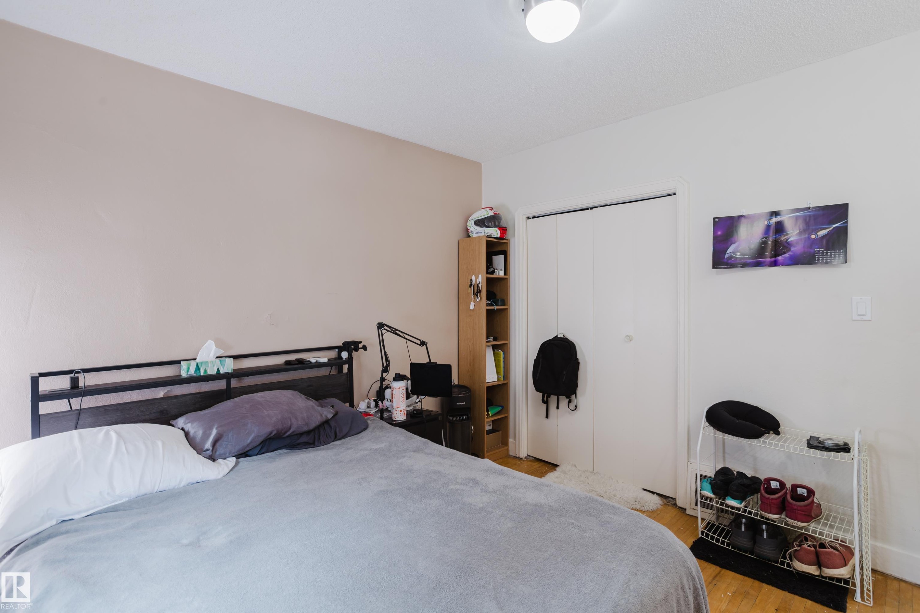Bedroom featuring light wood-finish flooring, a built-in closet with bi-fold doors, and a ceiling-mounted light fixture - 11158 65 Street, Edmonton, AB