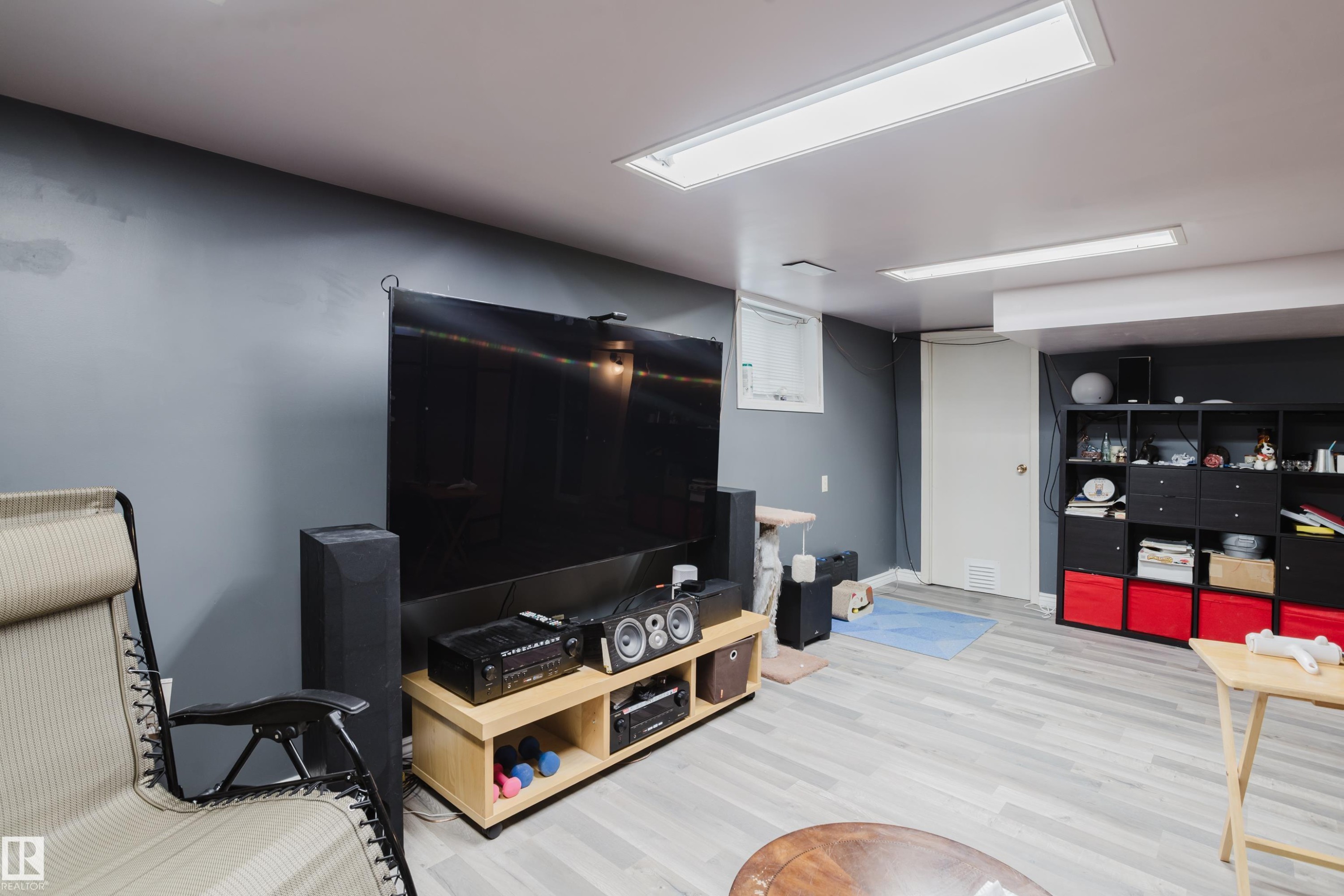 Versatile recreation room featuring light wood-finish flooring, dark accent walls, and white ceiling panels with integrated linear lighting - 11158 65 Street, Edmonton, AB