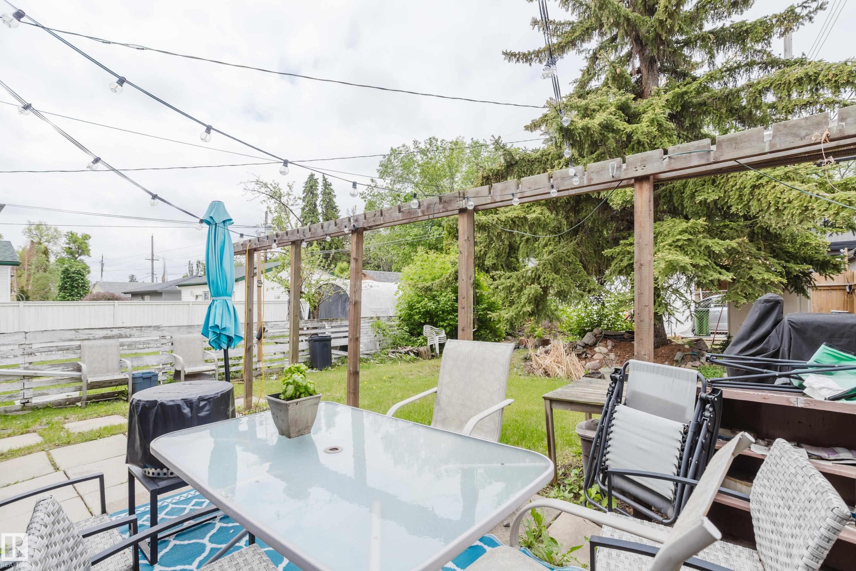 Expansive backyard featuring a wood pergola, string lighting, mature trees, and a combination of paved patio and grassy areas - 11158 65 Street, Edmonton, AB