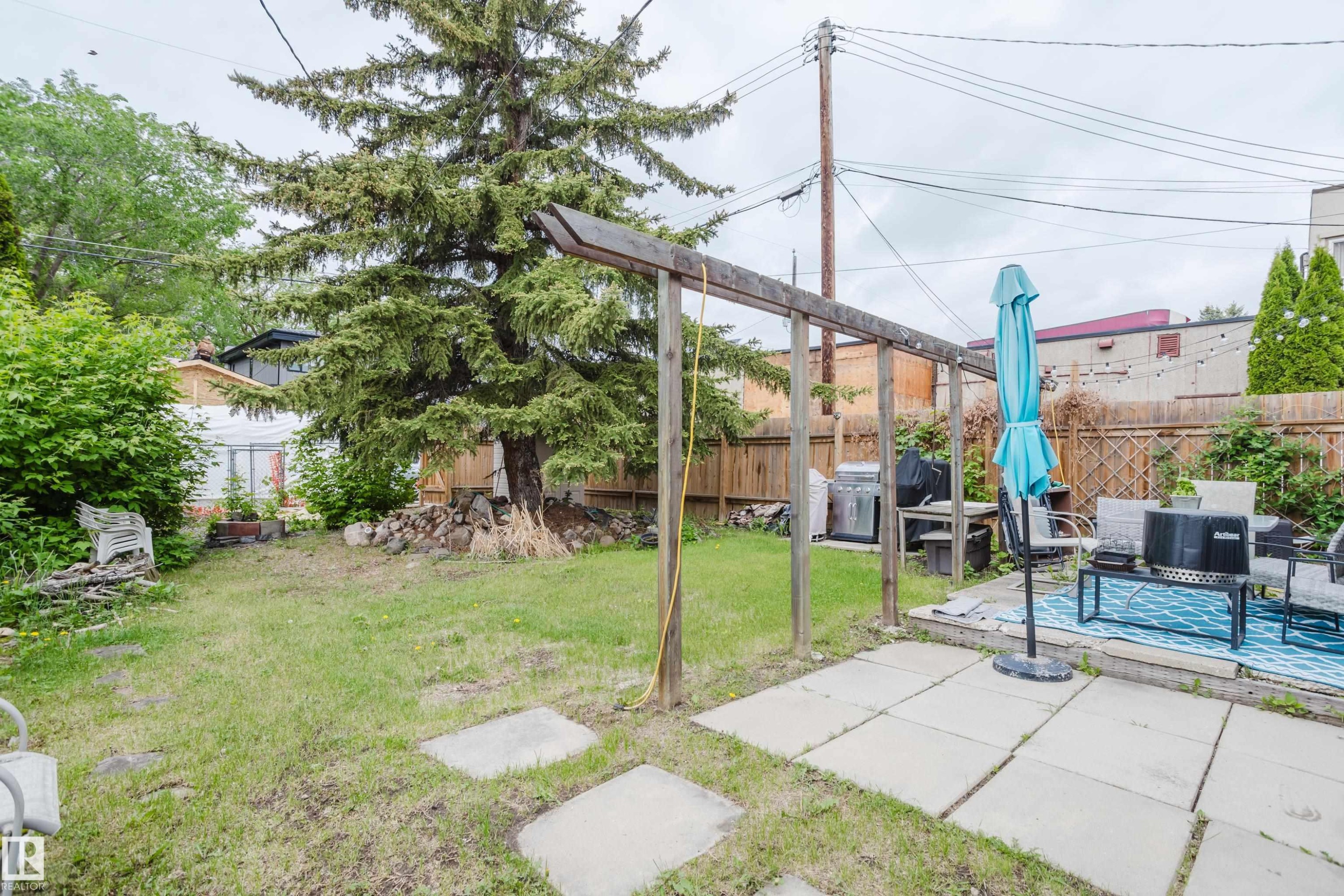 Spacious backyard featuring a concrete patio with stepping stones, a wooden pergola structure, a mature evergreen tree, and wood fencing - 11158 65 Street, Edmonton, AB
