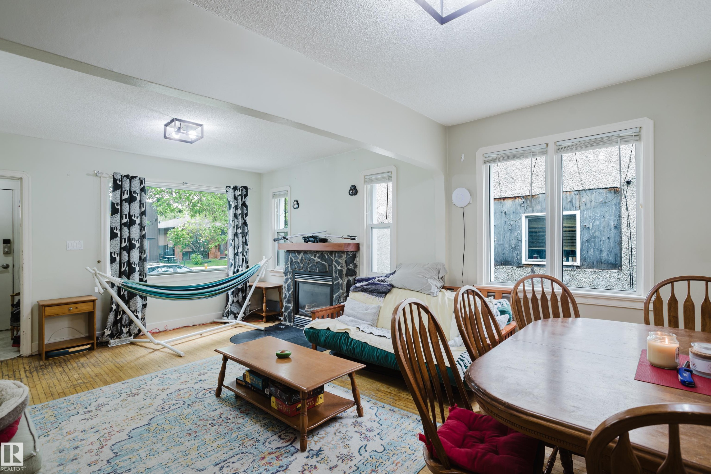 Spacious living area featuring wood-finish flooring, a decorative fireplace with stone surround, and multiple windows - 11158 65 Street, Edmonton, AB
