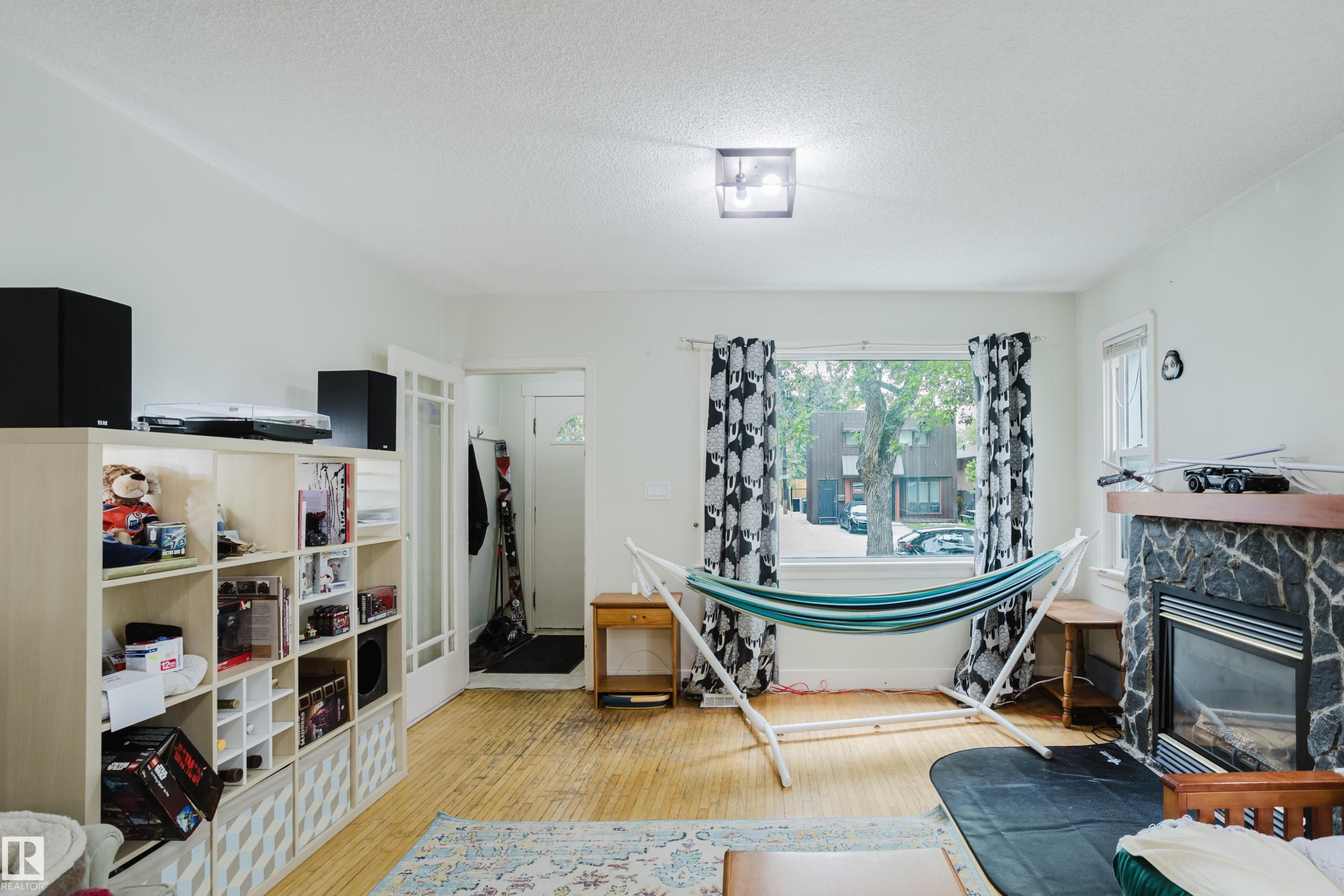 Living area featuring wood-finish flooring, a large window, and a stone-surround fireplace with a wood mantle - 11158 65 Street, Edmonton, AB