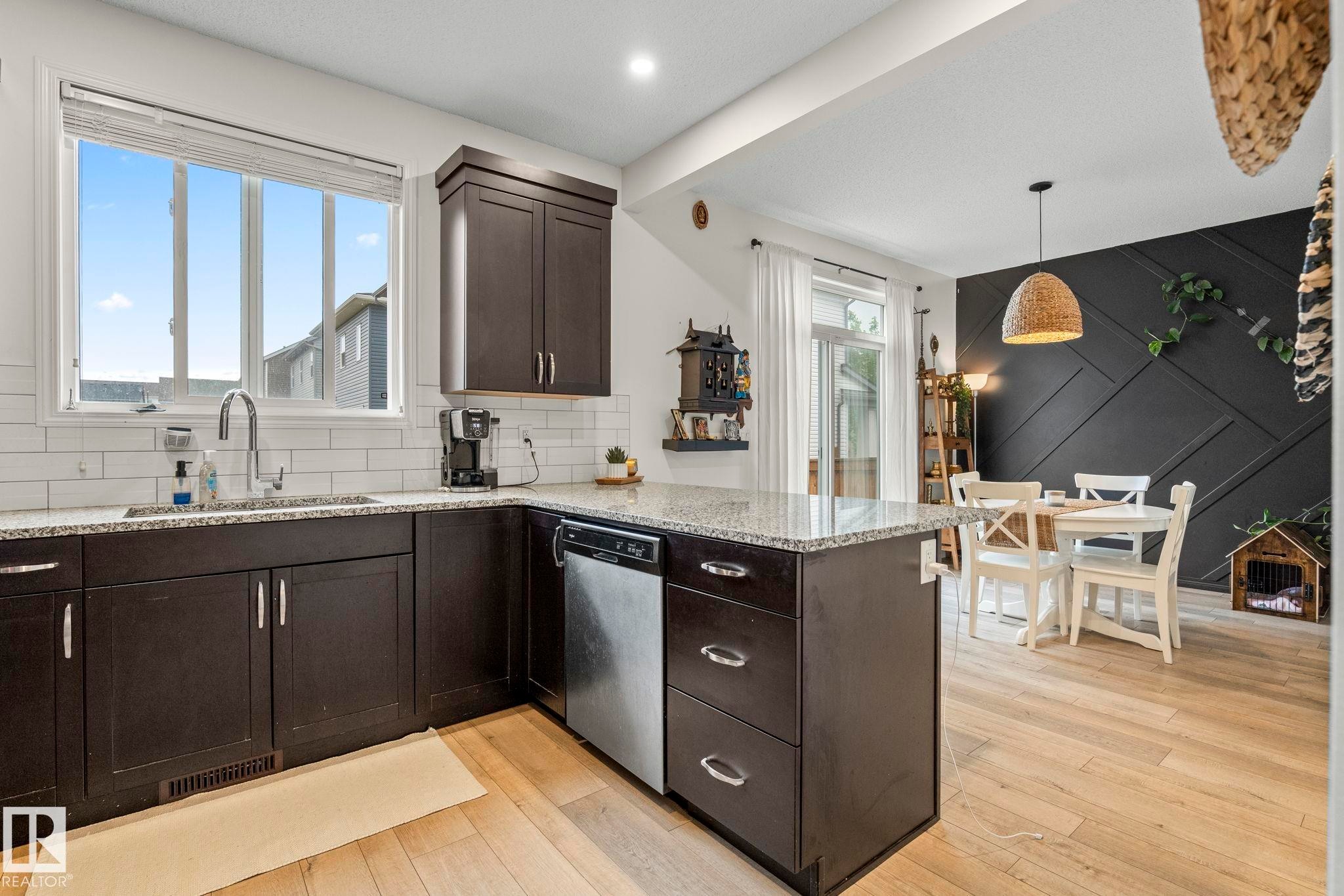 Kitchen and dining area featuring dark wood cabinetry, light granite countertops, and a white subway tile backsplash - 20227 17Ave, Edmonton, AB